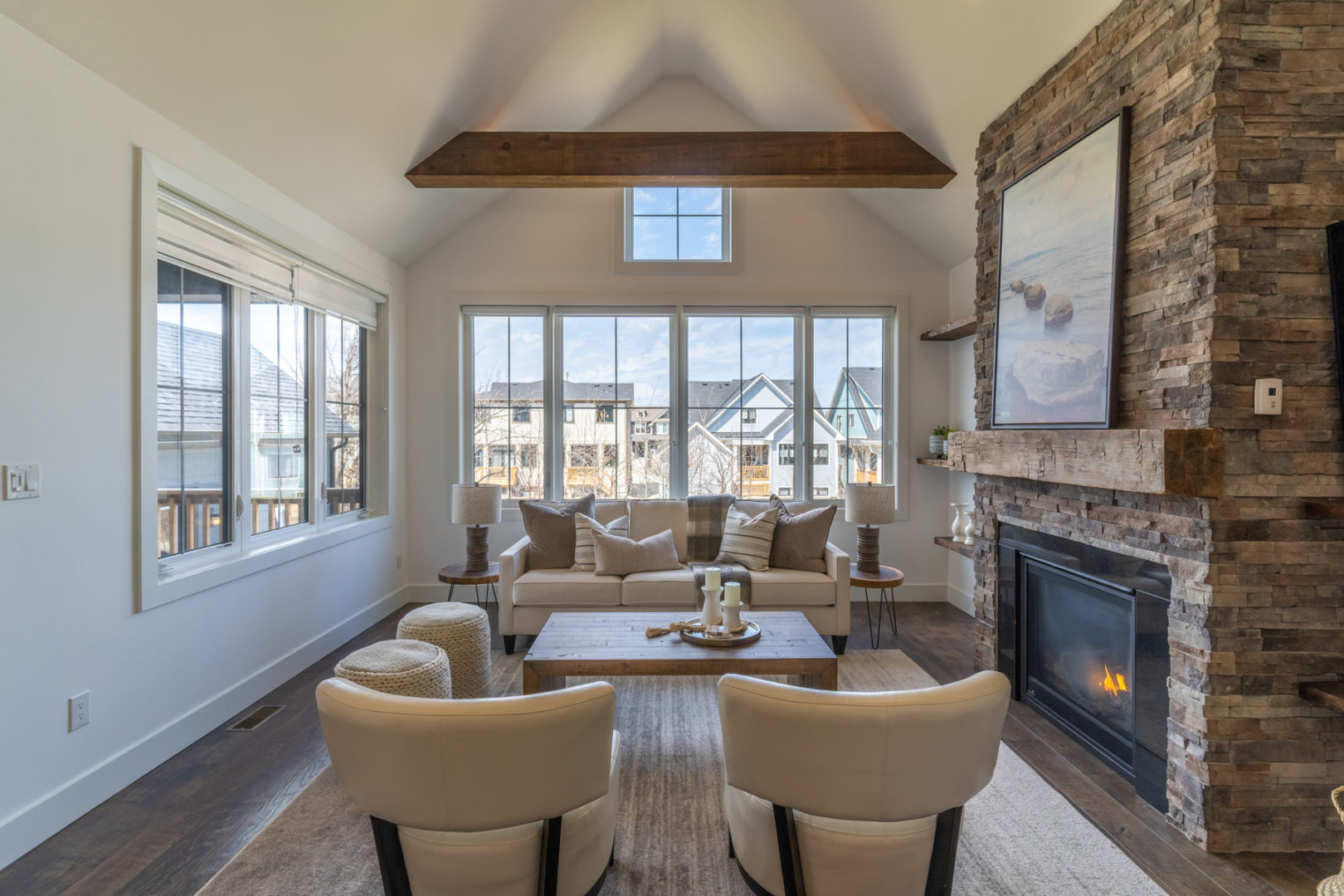 A bright living room area with large windows, a fireplace, two chairs and a couch.