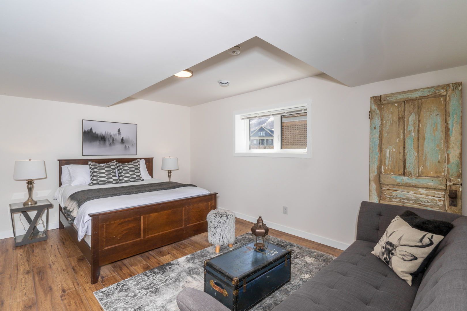 A basement bedroom with a big bed and a small window.
