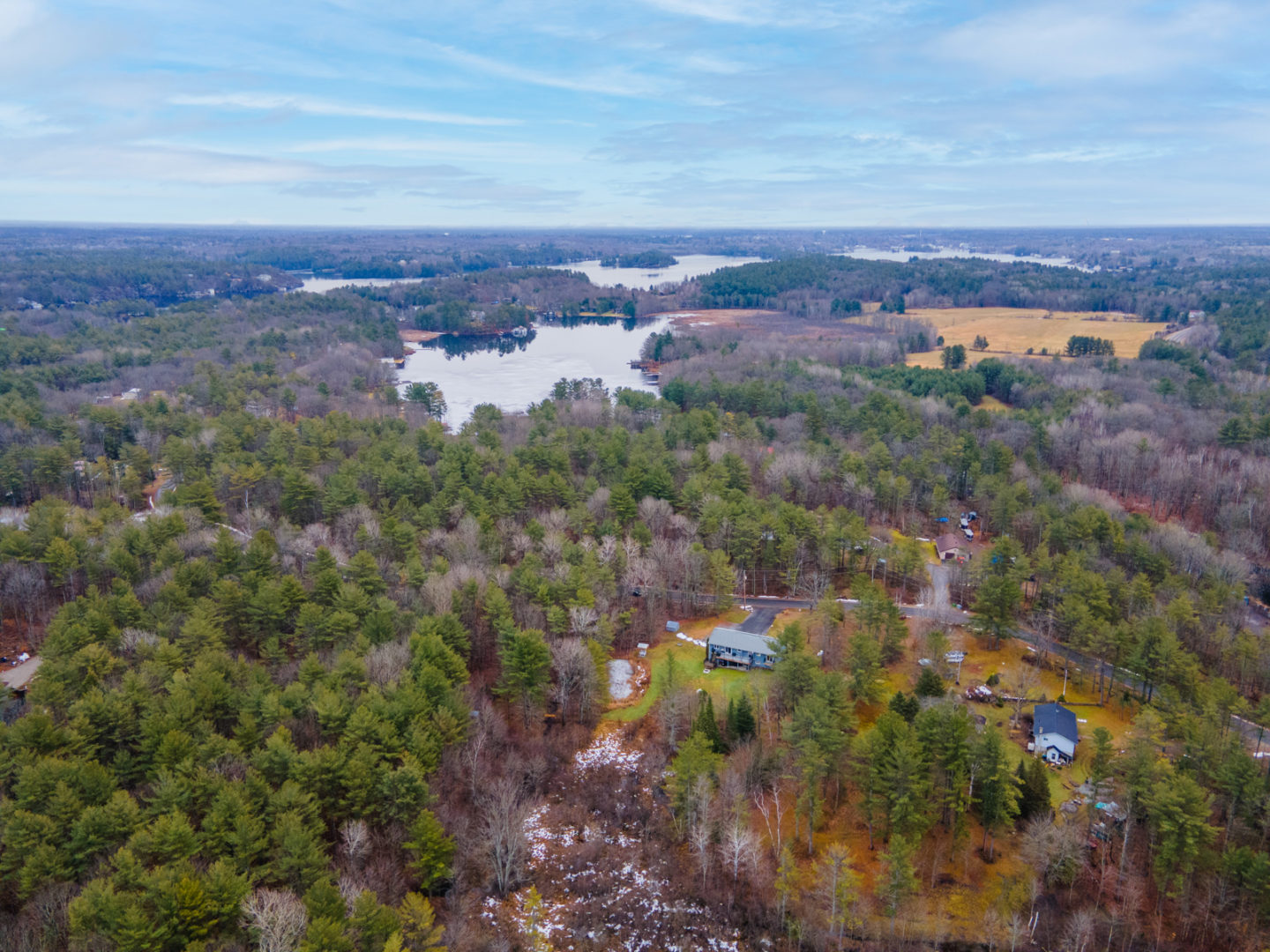 Overhead view of a rural area with lots of trees and lakes in the background. A small home can be seen below.