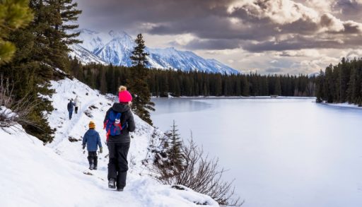 A group of people walking on a winter hiking trail along Johnson Lake in Banff National Park Canada