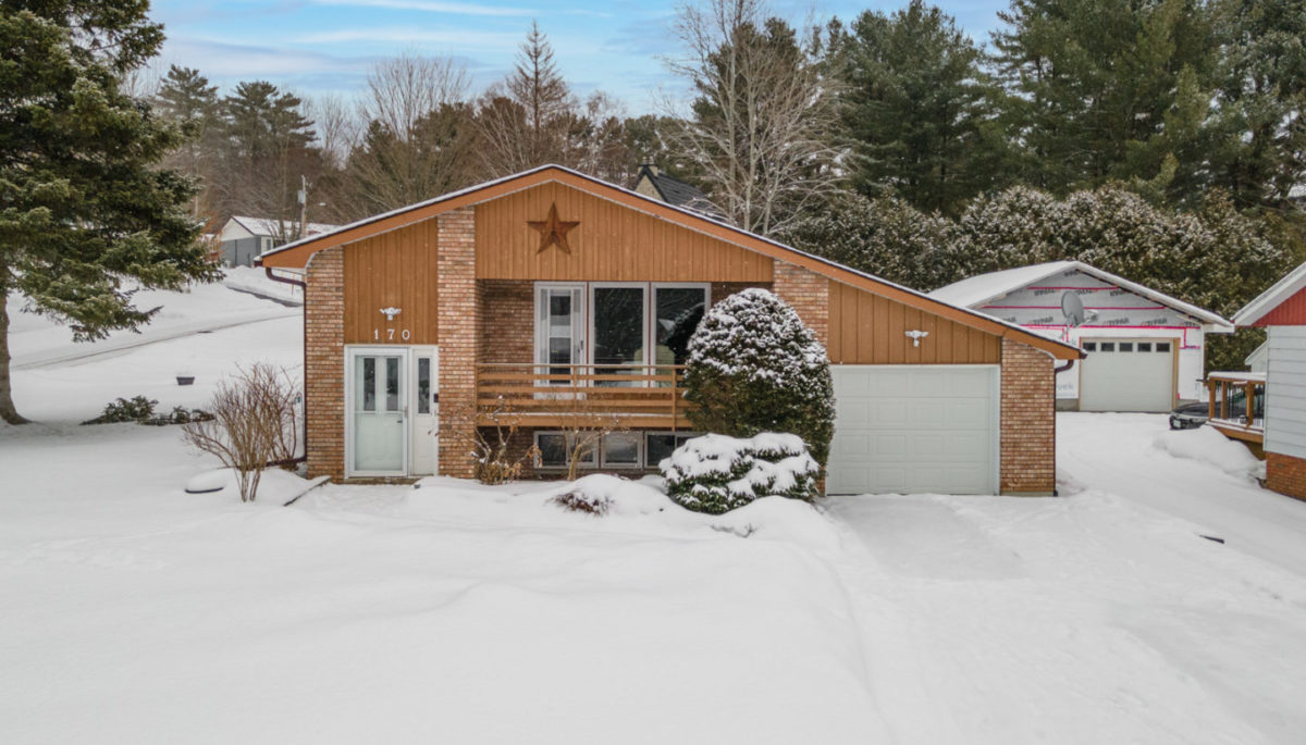 The front of a house with a single car garage and a front balcony, in a small neighborhood surrounded by trees.