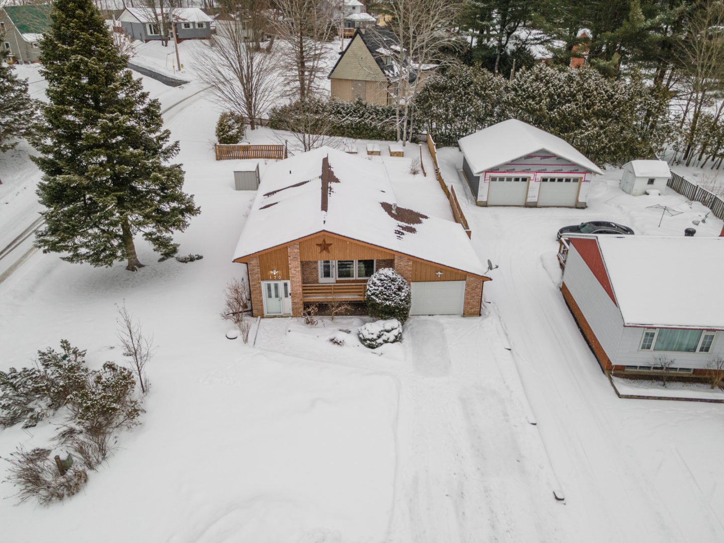 A view from above of an average-size house with a fenced in backyard, in a small neighborhood surrounded by trees.