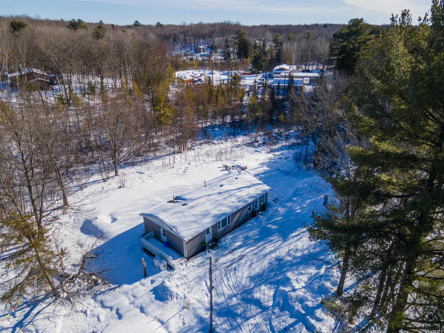 A small cottage bungalow surrounded by open snowy yard and then trees all around.