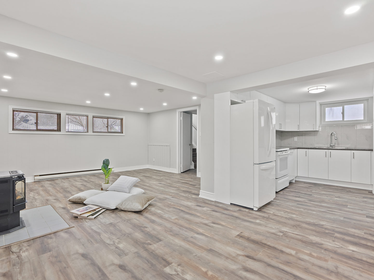 A bright, open, bare downstairs space with hardwood floors, a fireplace, and a small kitchen.