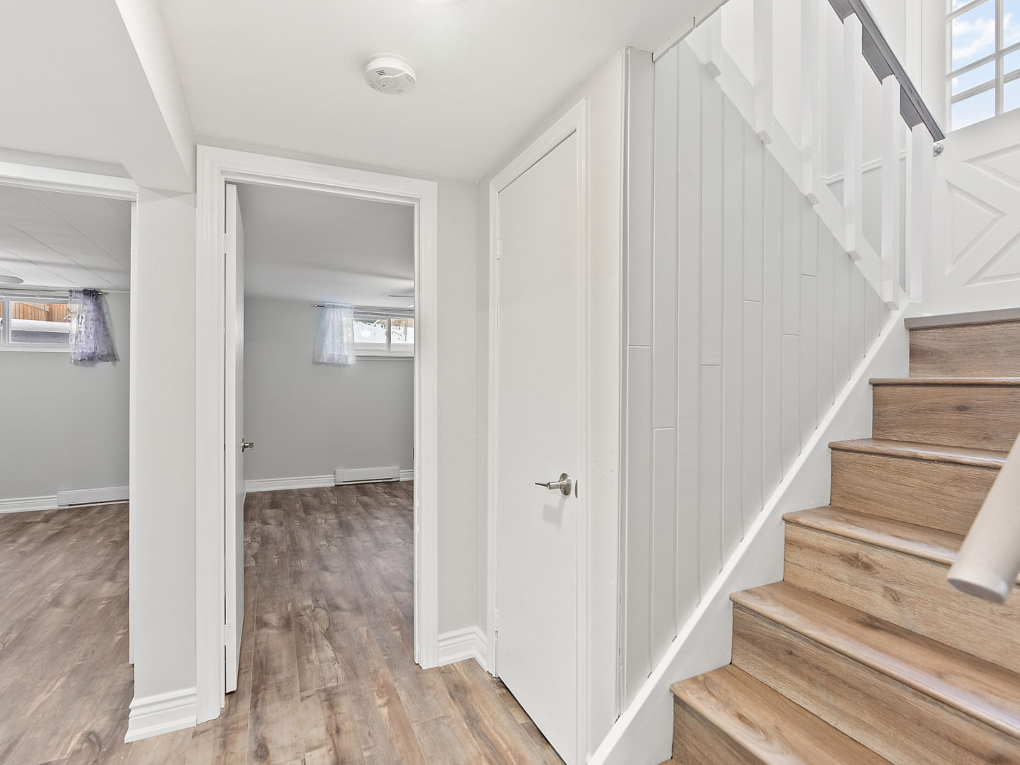 An area at the bottom of a staircase, with doorways leading into two empty bedrooms.