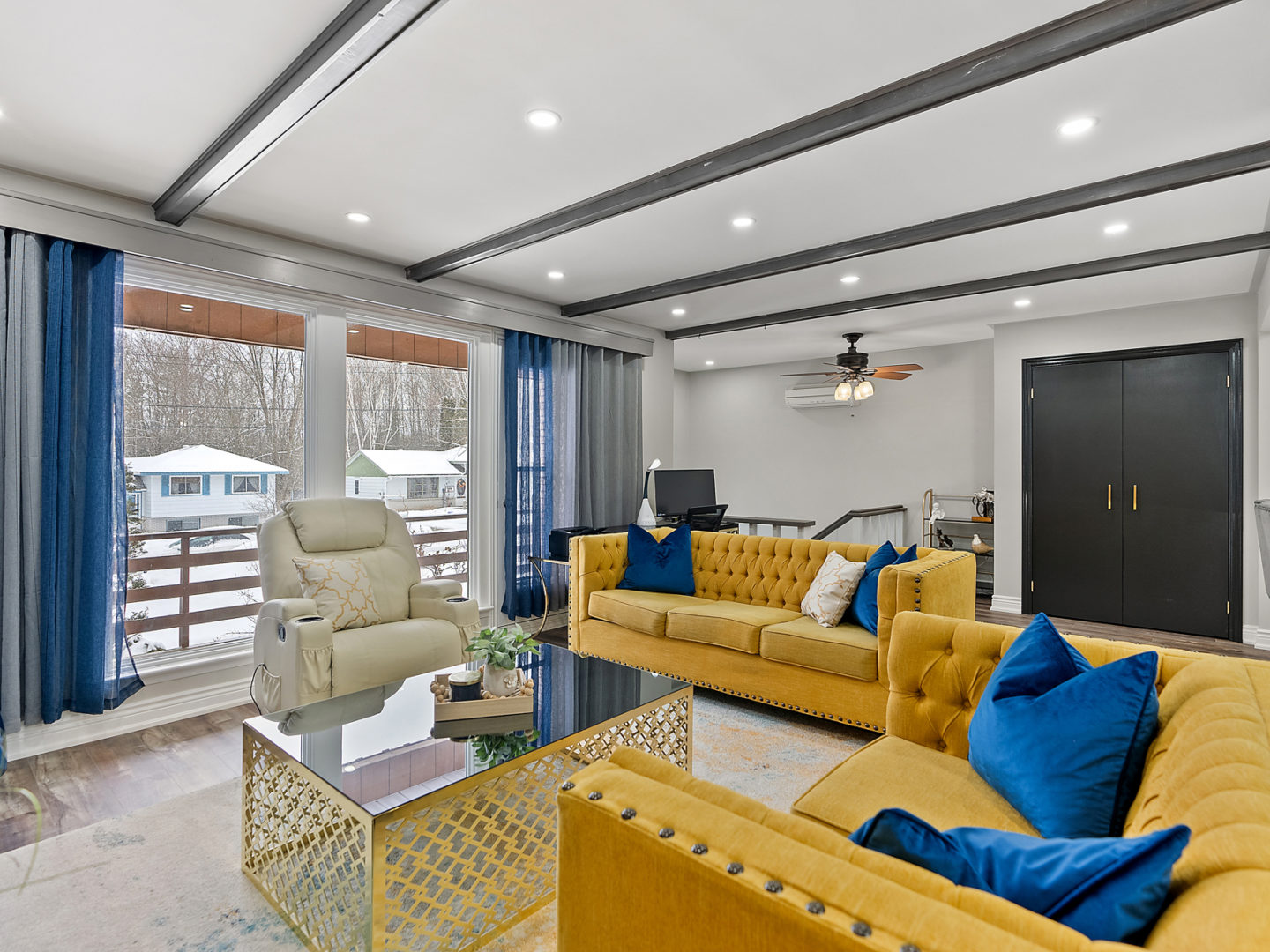 A bright living area with bold yellow seating and a large window looking out to houses across the street.
