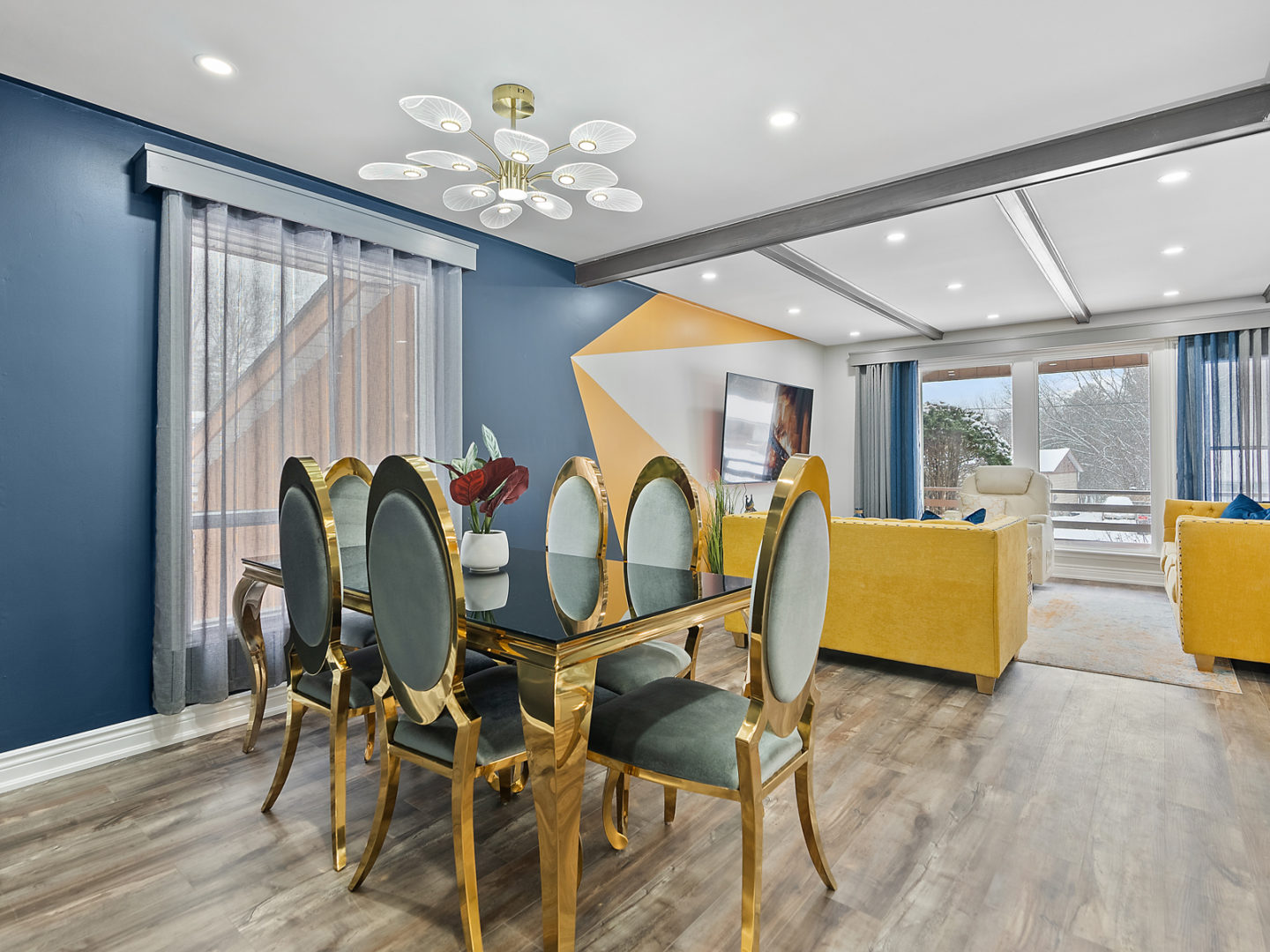 An open-concept space with a dining area that has a table and chairs, opening into a living area with seating. Large windows fill the space with light.