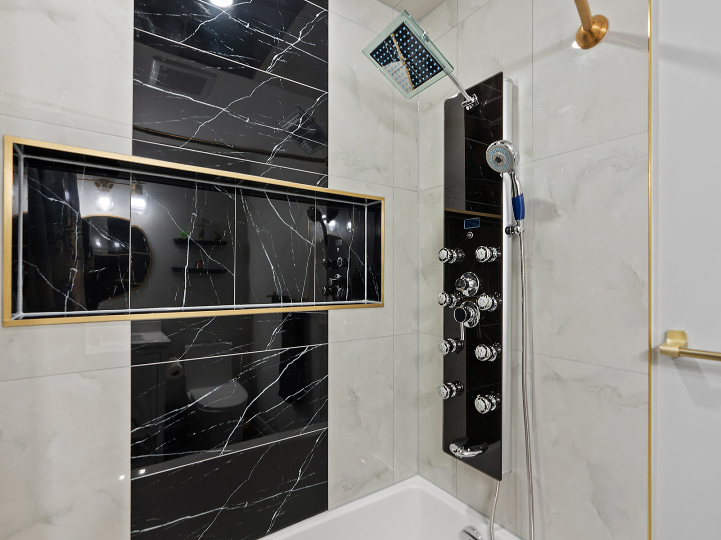 A shower in a bathtub, with black accent tiles on the walls.