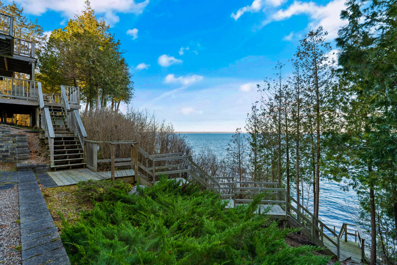 A large wooden staircase weaves down a hilly forest area, leading from a big lake house to the waterfront.