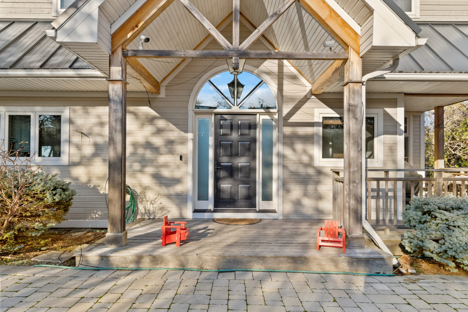The front porch area of a large house, with a black front door surrounded by windows. A triangular covering supported by wooden beams extend over the front door area.