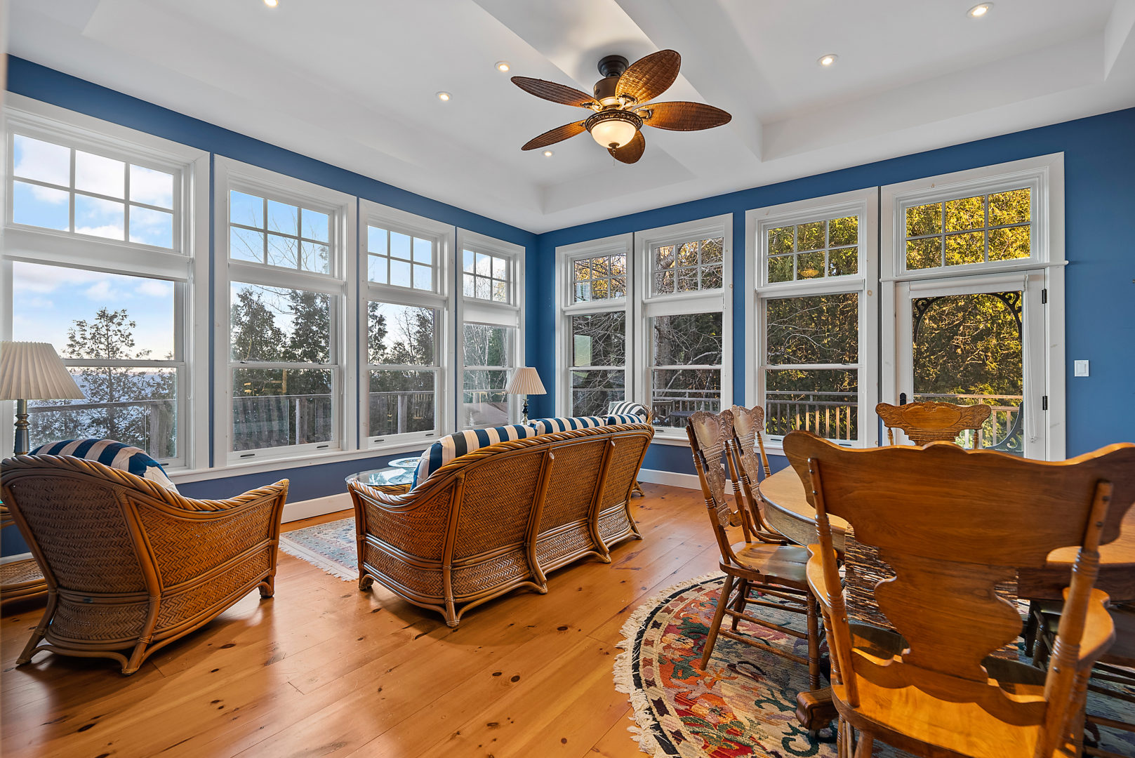 A bright dining room with a table and chairs that has a couch sitting area off to the side. The walls are painted dark blue and are full of windows.