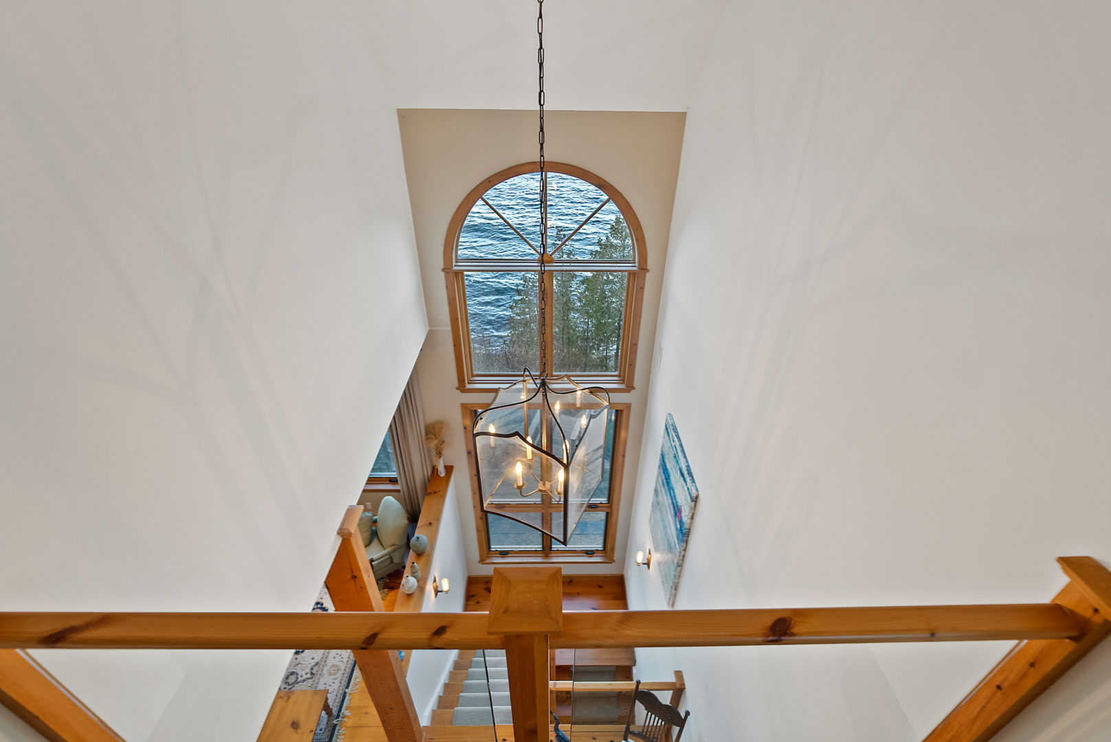 A view over a second-floor landing, looking out to a floor-to-ceiling window and a living space down below.