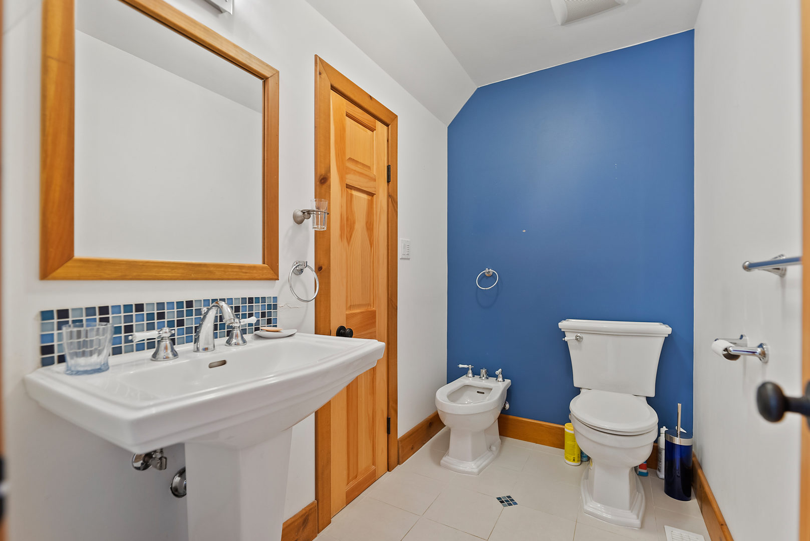 A small area with a toilet, a sink, and a blue accent wall, off a larger bathroom.