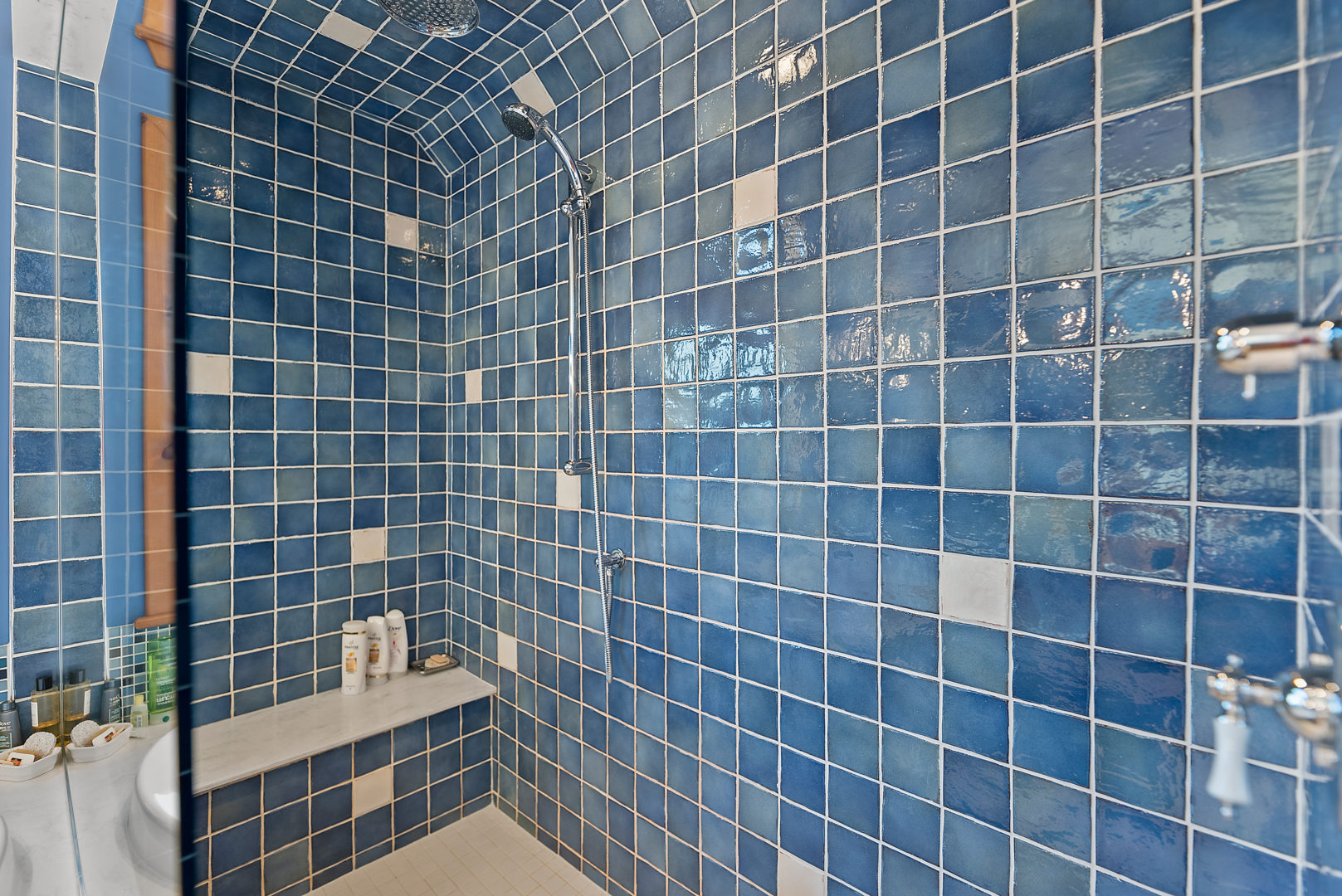 A large walk-in shower with a glass door and blue tile walls.