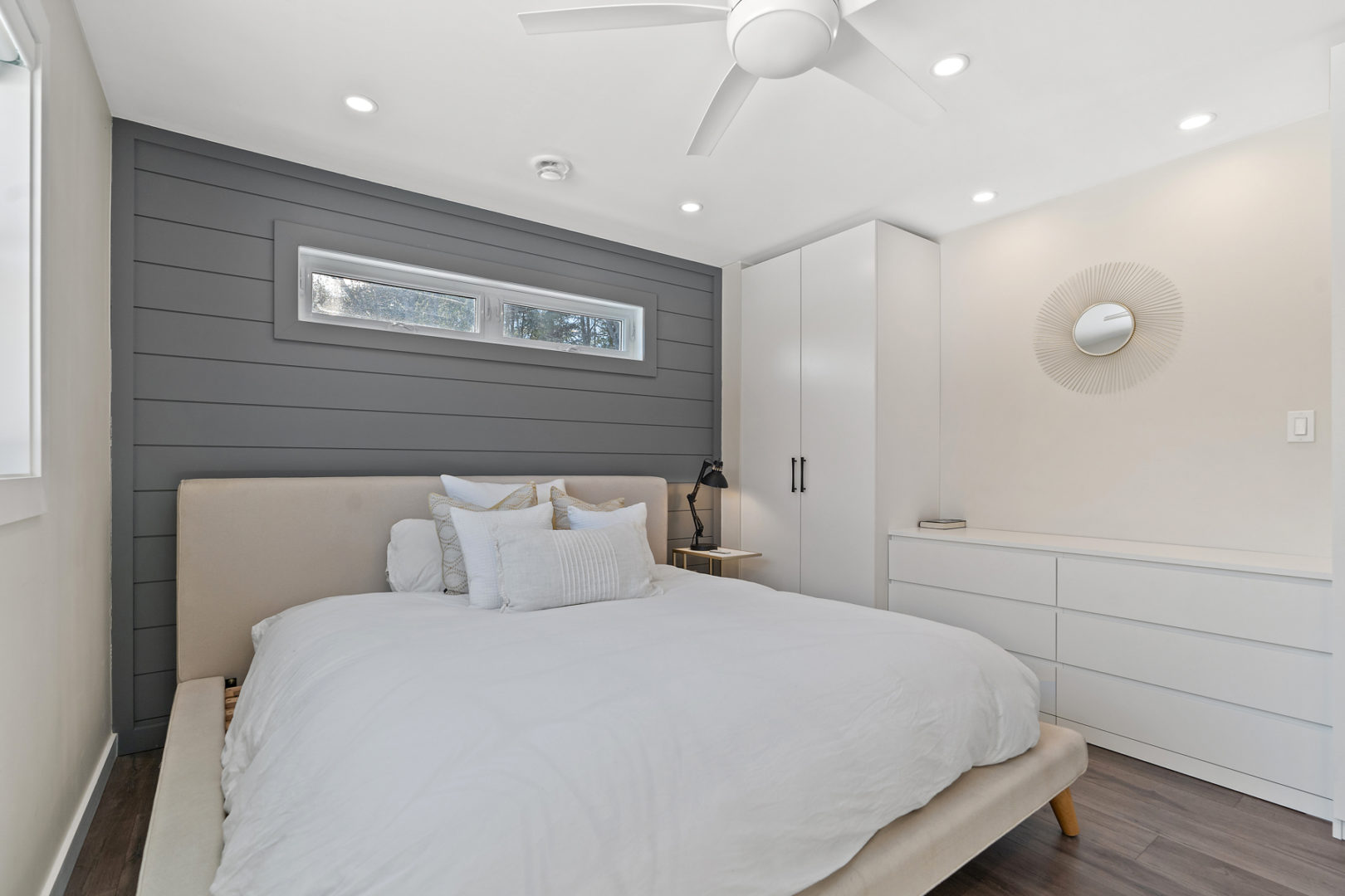 A bright bedroom with a big bed and an abundance of cabinet and drawer space built into the wall.