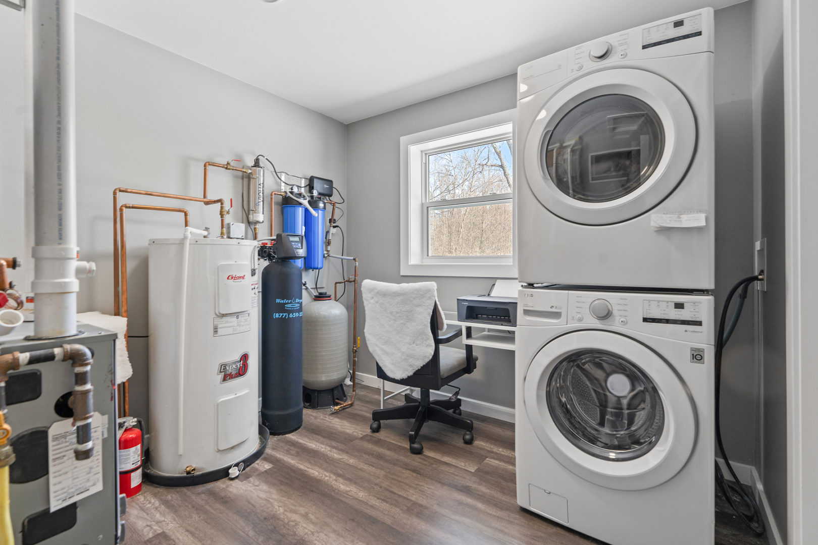 A small room with a furnace and water heater, laundry machines, and a small workspace with a desk.