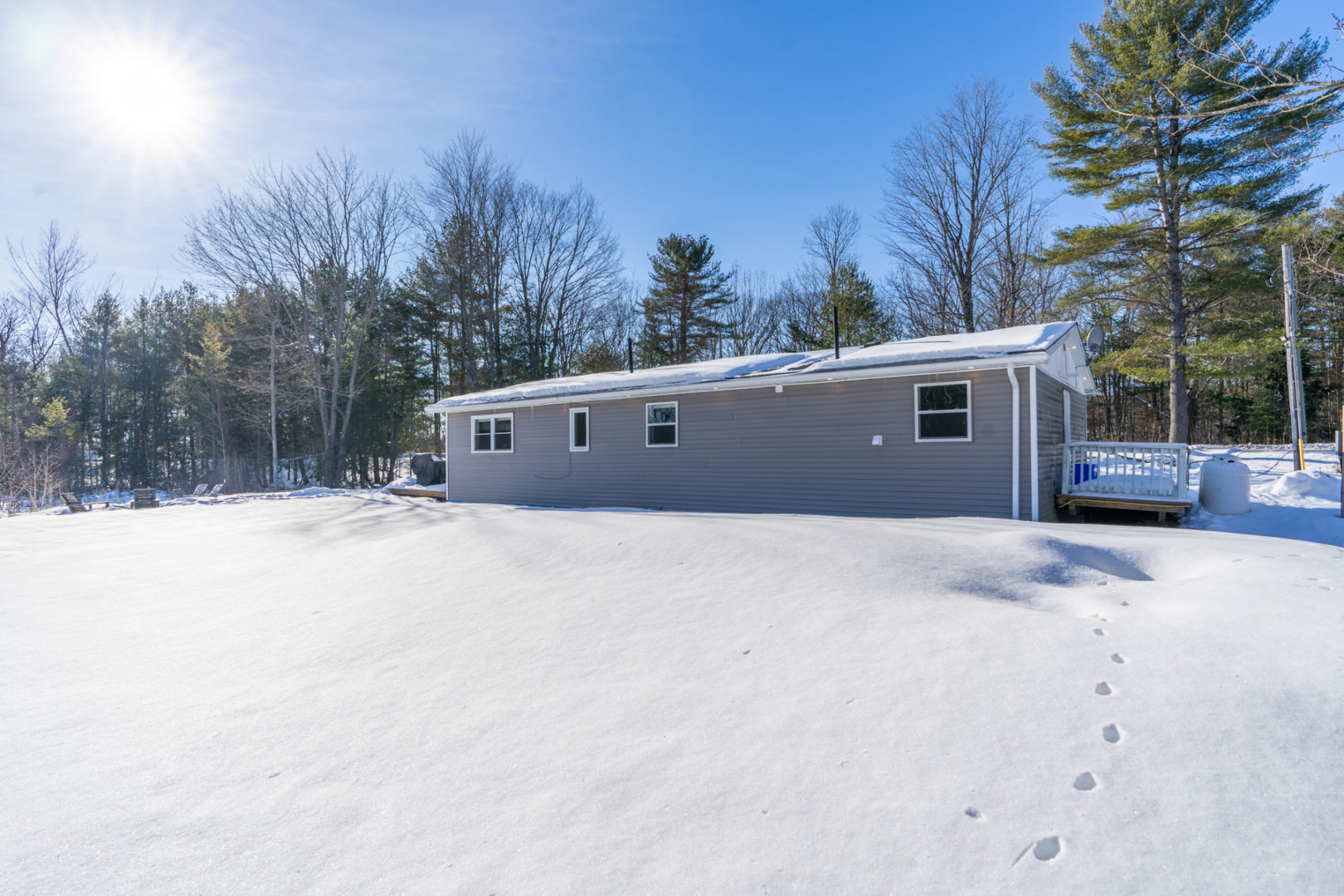 The back of a modest-sized cottage bungalow, with a large, open snowy yard and trees all around.