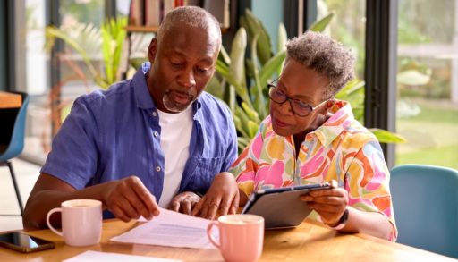Senior Couple Sitting Around Table At Home Reviewing Finances Using Digital Tablet, considering renegotiating their mortgage