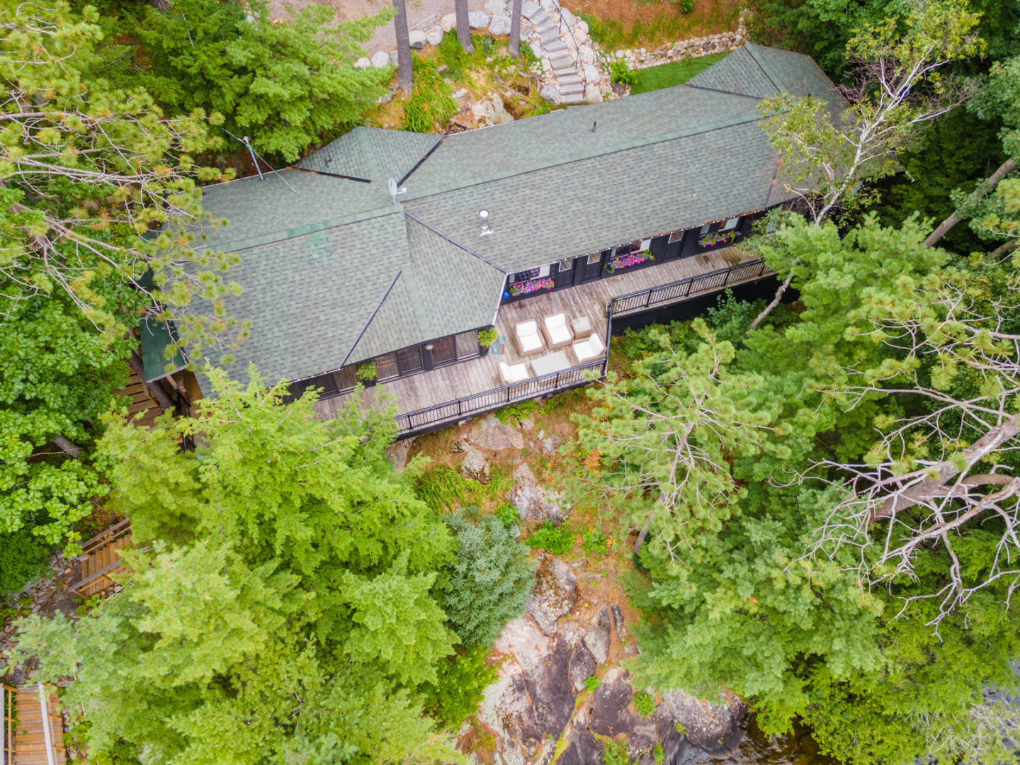 Overhead view of a large cottage with a wrap-around deck, surrounded by trees.