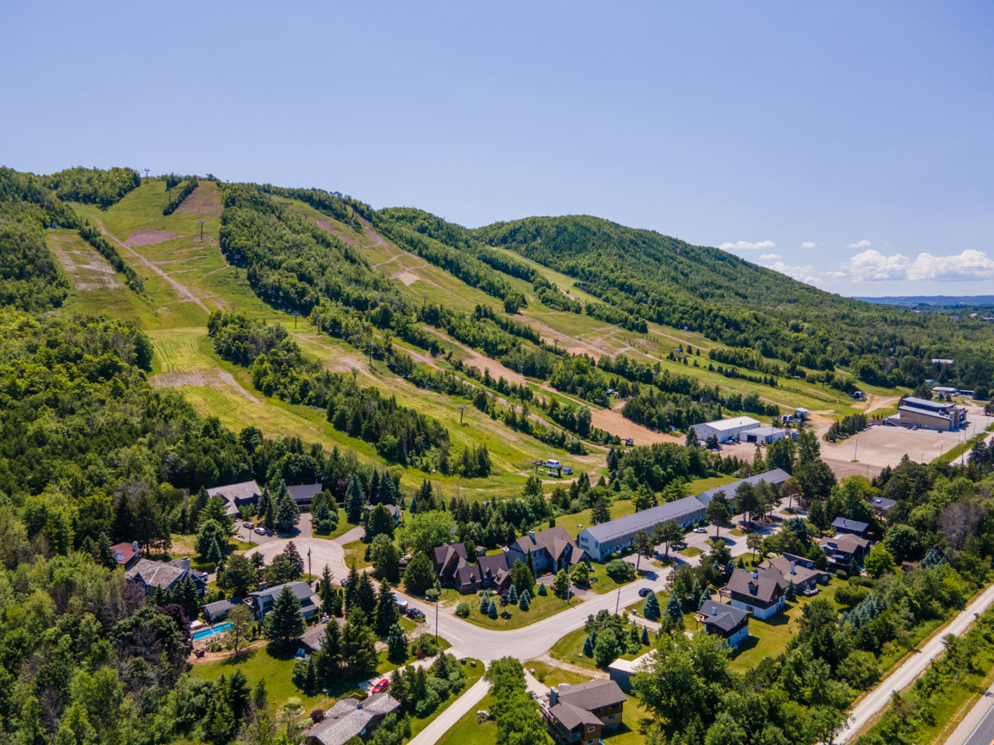 A sloping mountain covered in trees, with paths for ski slopes going down. At the base of the mountain is a small residential neighbourhood.