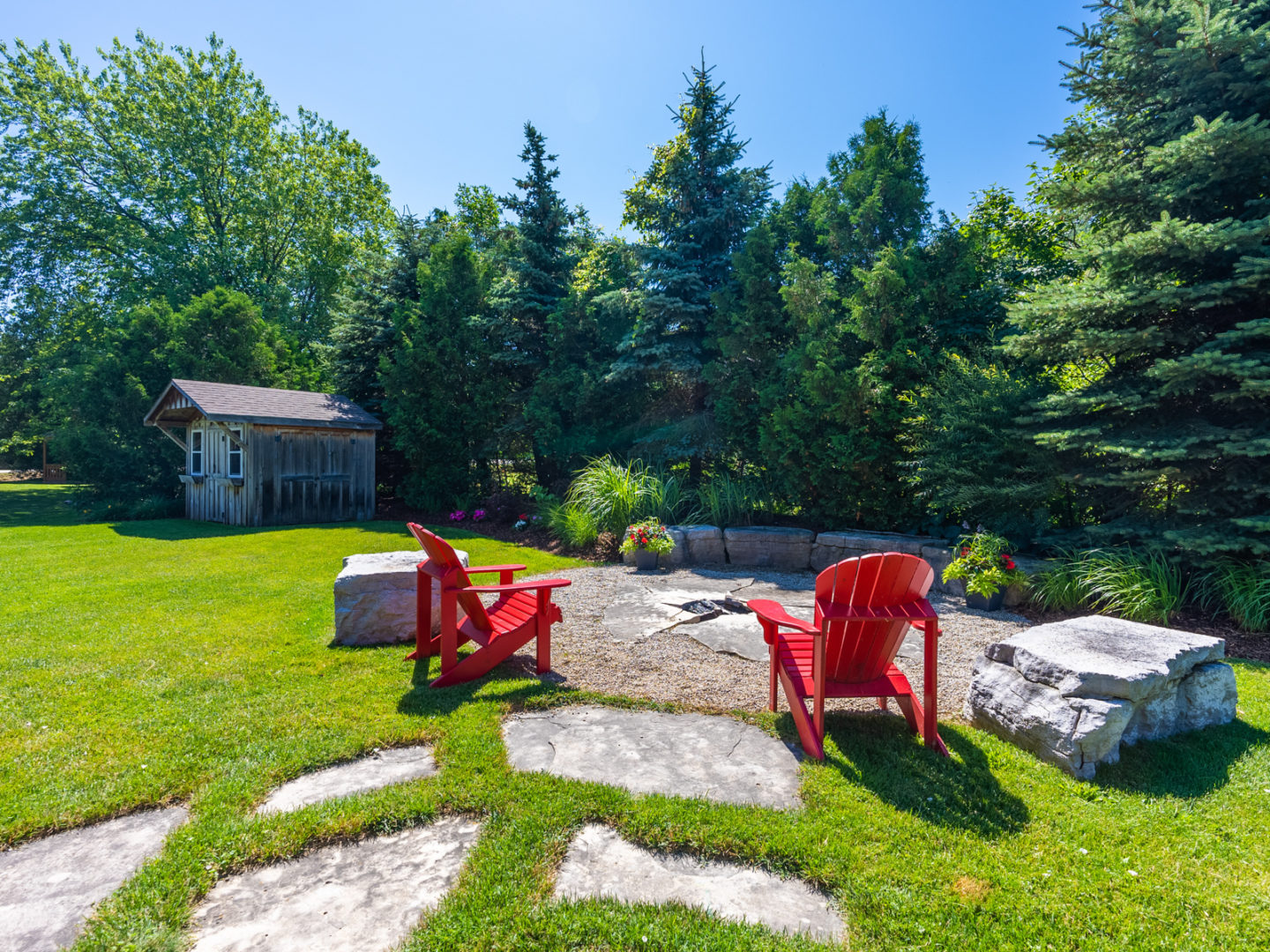 A large patio area with a fire pit that has two Muskoka chairs around it.