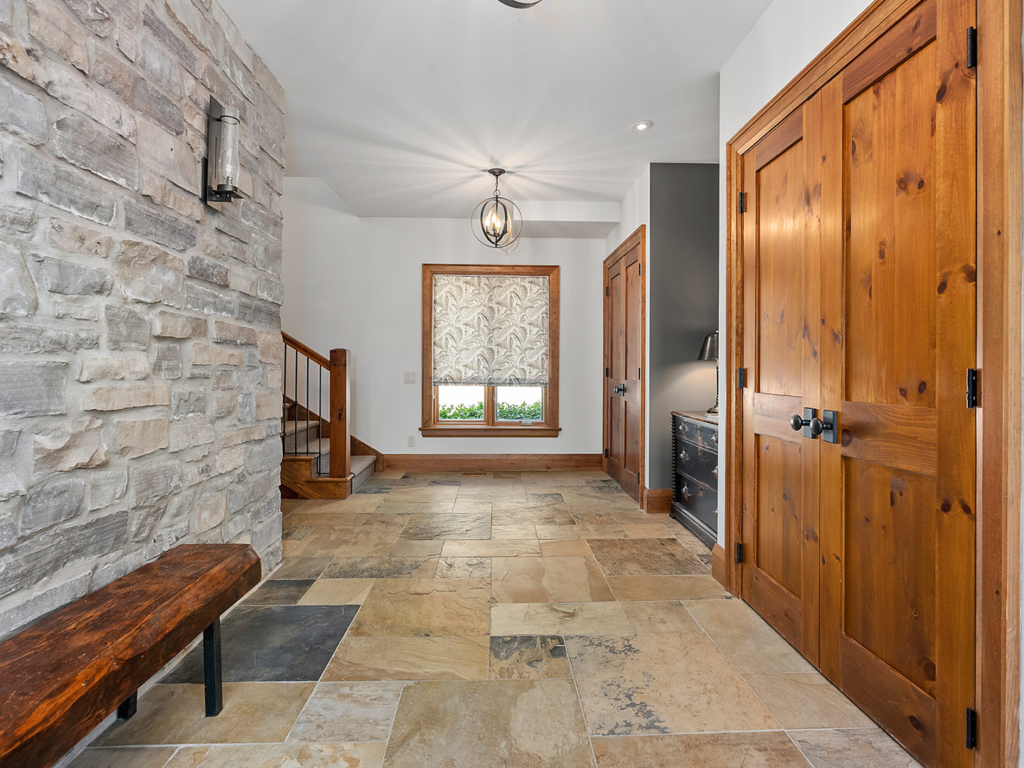Inside the front entrance of a large home, facing toward the stairway. The foyer is wide, and there is a stone accent wall.