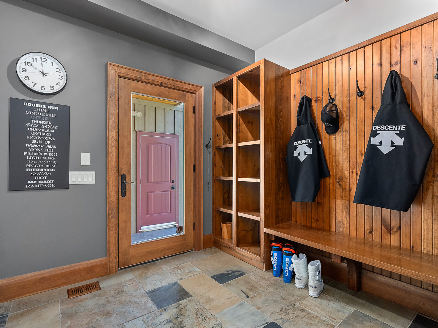 A mudroom area with tiled floors, a wall with a bench, hooks, and cubby storage space, and a large door leading outside.