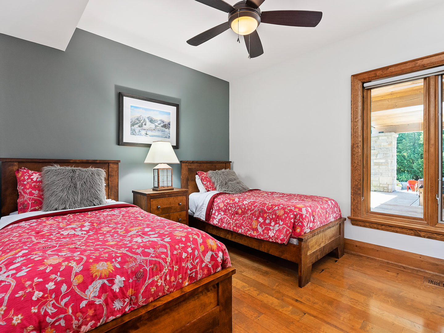 A medium sized bedroom with two small beds, hardwood floors, and a large window.