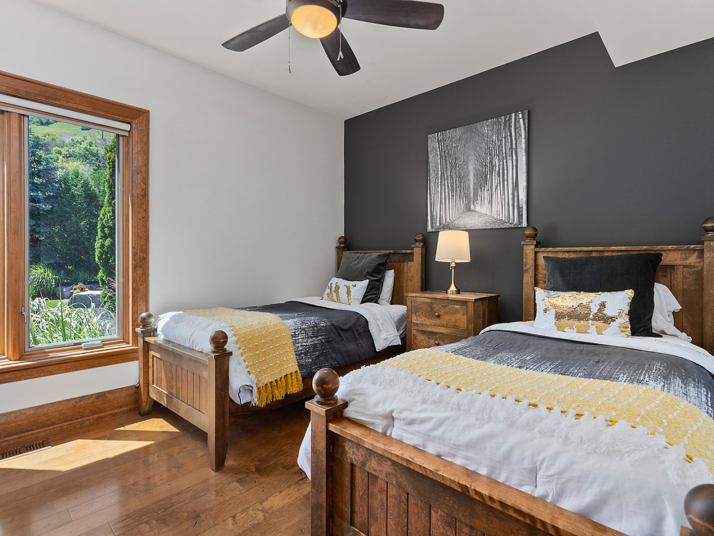 A medium sized bedroom with two double beds, hardwood floors, and a ceiling fan.
