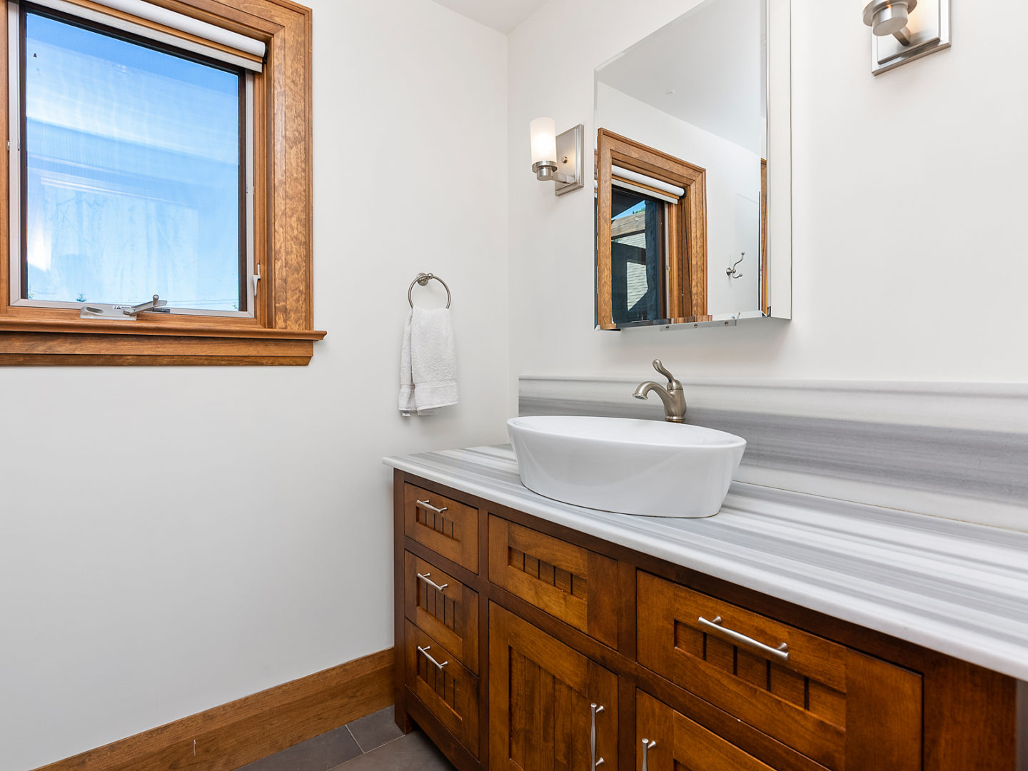 A nice bathroom sink with white countertops and dark brown cupboards below.