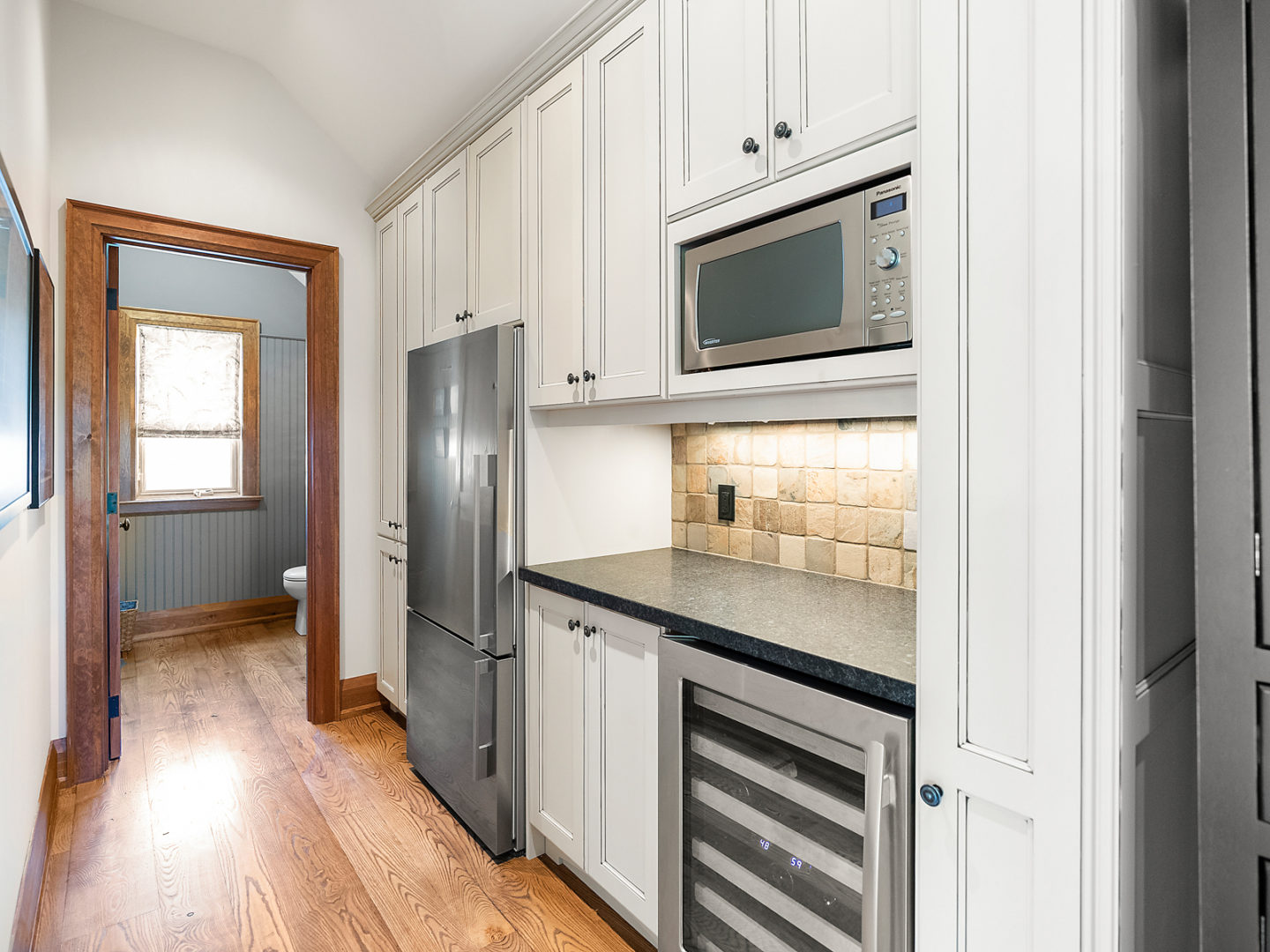 A small hallway with pantry storage and an extra fridge, leading to a small powder room.