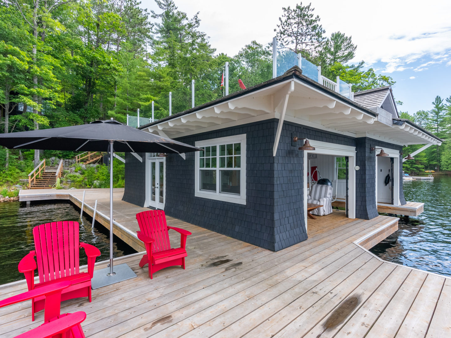 A boutique boathouse with a large dock, lots of windows, and a rooftop deck area.