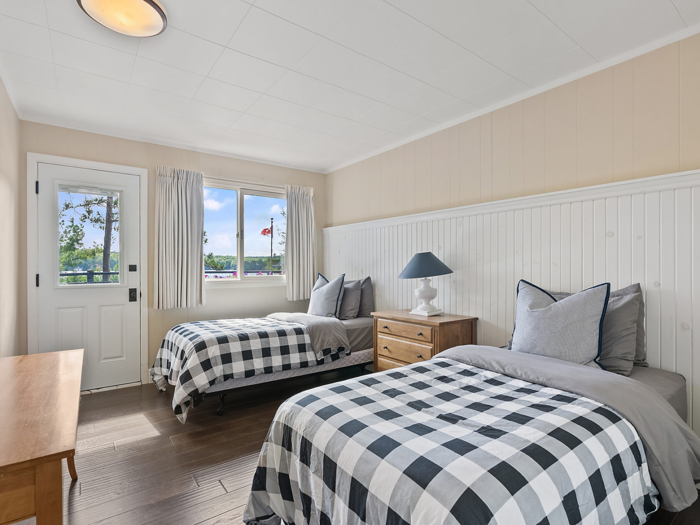 A bright bedroom with two beds and a door leading to an outdoor deck.