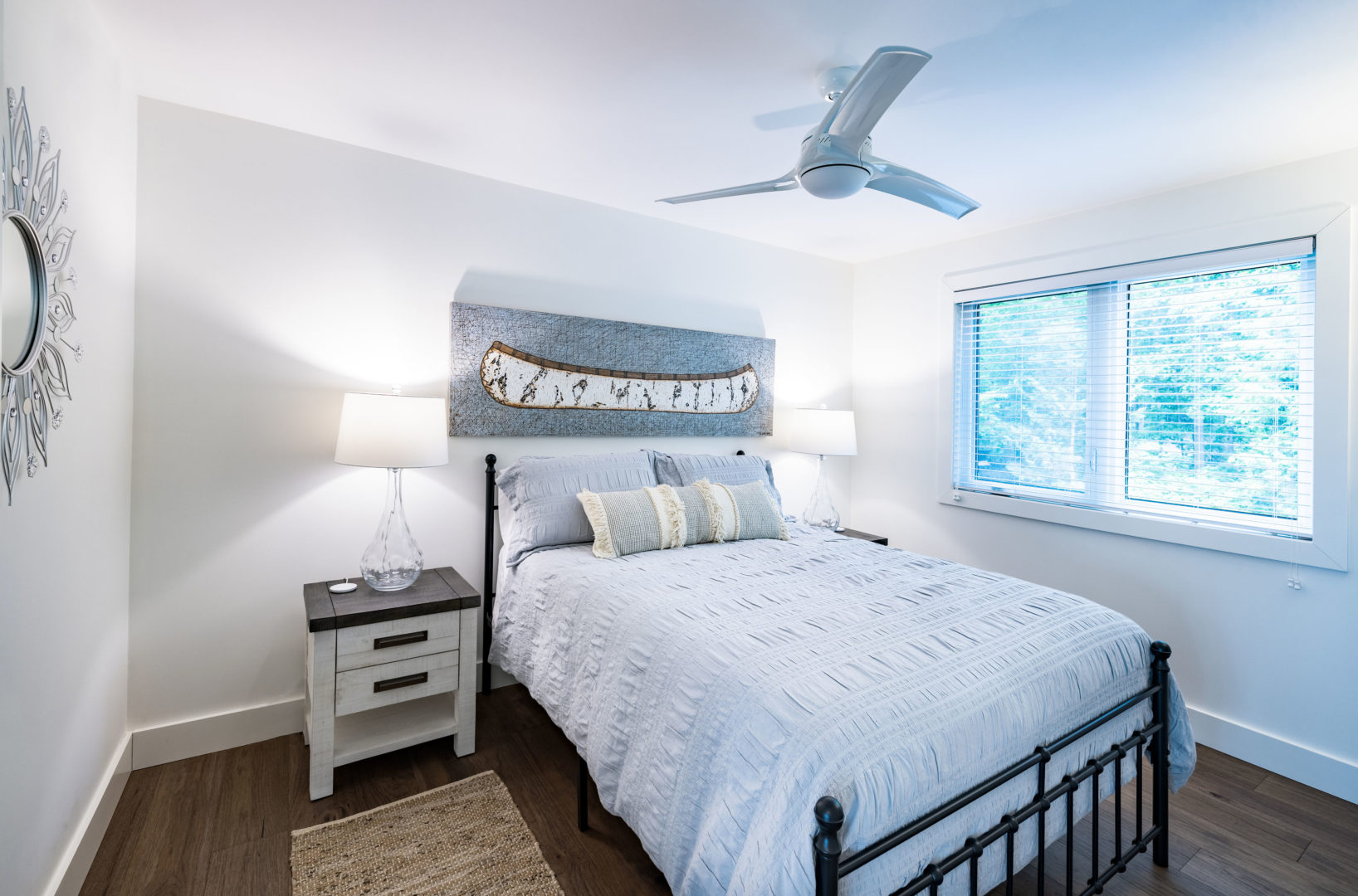A bright, simple bedroom with a bed, a ceiling fan, and a big window.