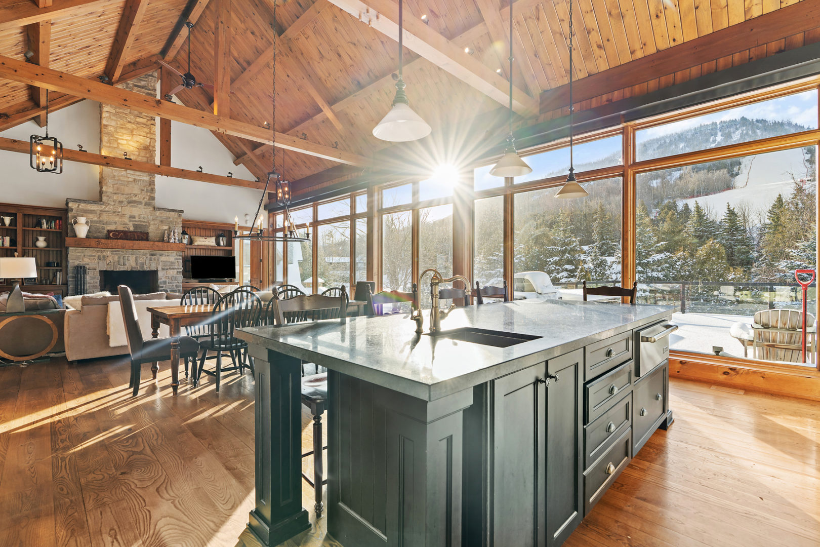 A large kitchen island in a huge open-concept space. Wooden beams accent the high ceiling, and windows with a mountain view stretch all along one side of the house.