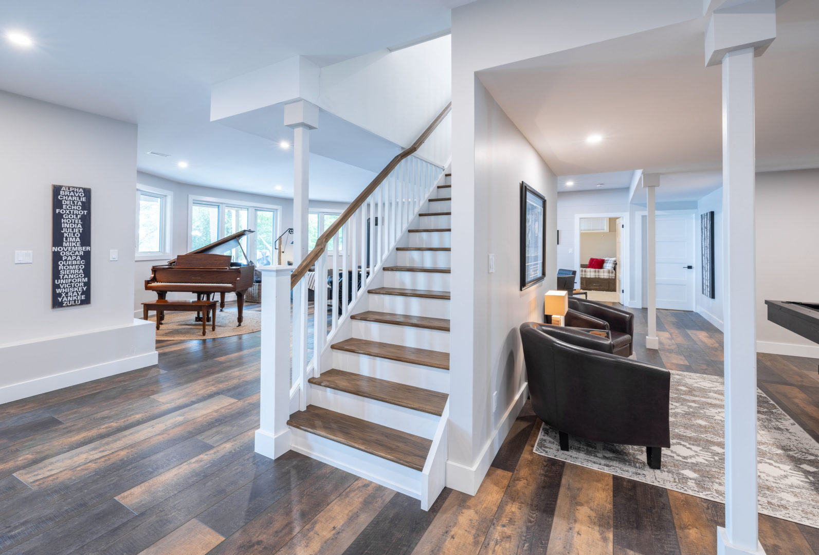 A bright, finished basement space that has walkout access to a backyard. Hardwood floors, a piano and chairs complete the space.
