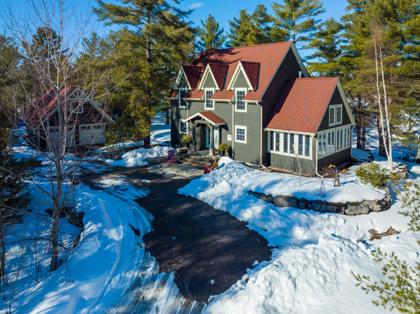 Driveway up to a large lakefront home, which has a greenish grey exterior and a red roof.