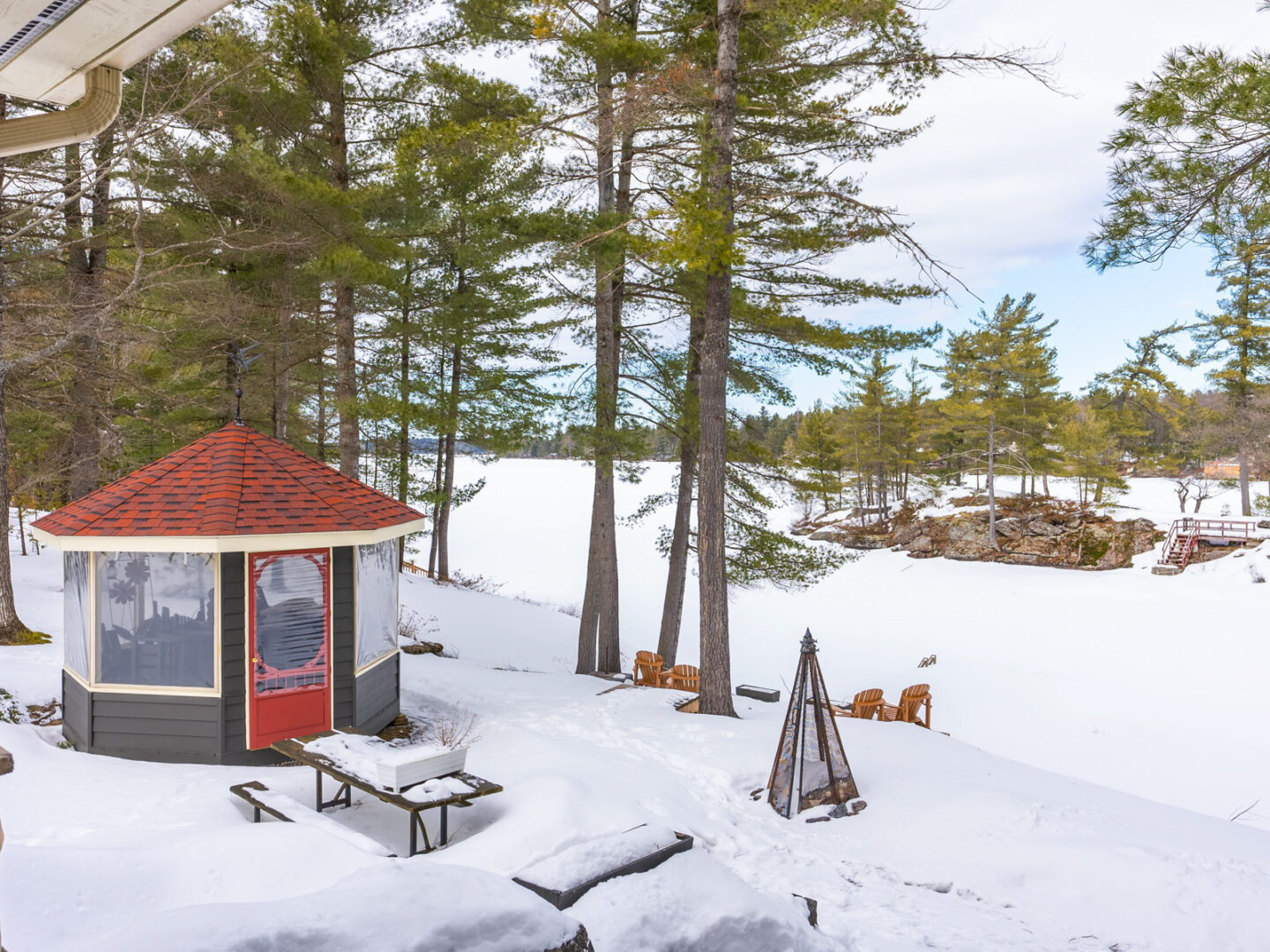 A small gazebo with a red roof, sitting on a snowy waterfront.