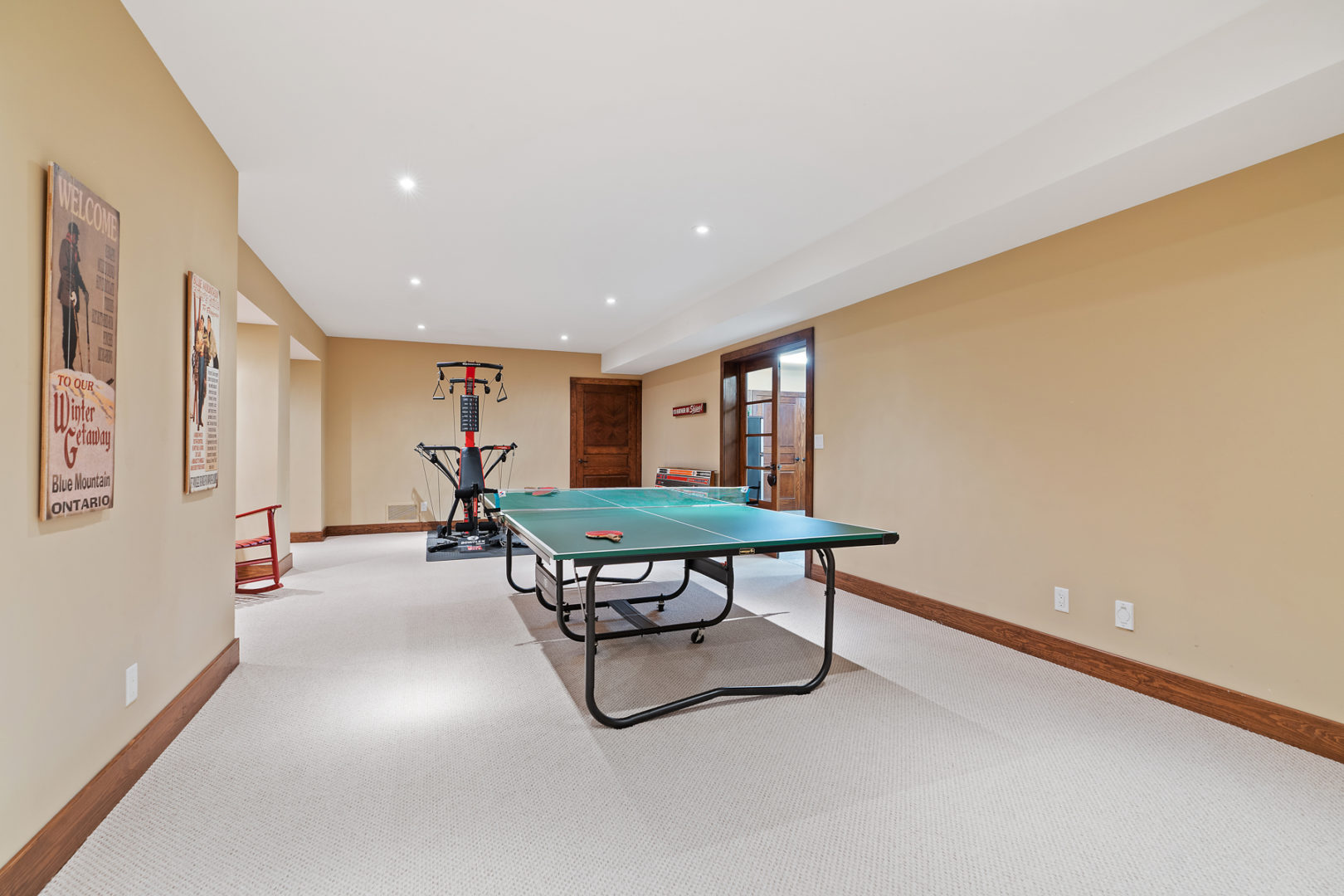 A large finished basement space of a luxury home, with a ping pong table and gym equipment.