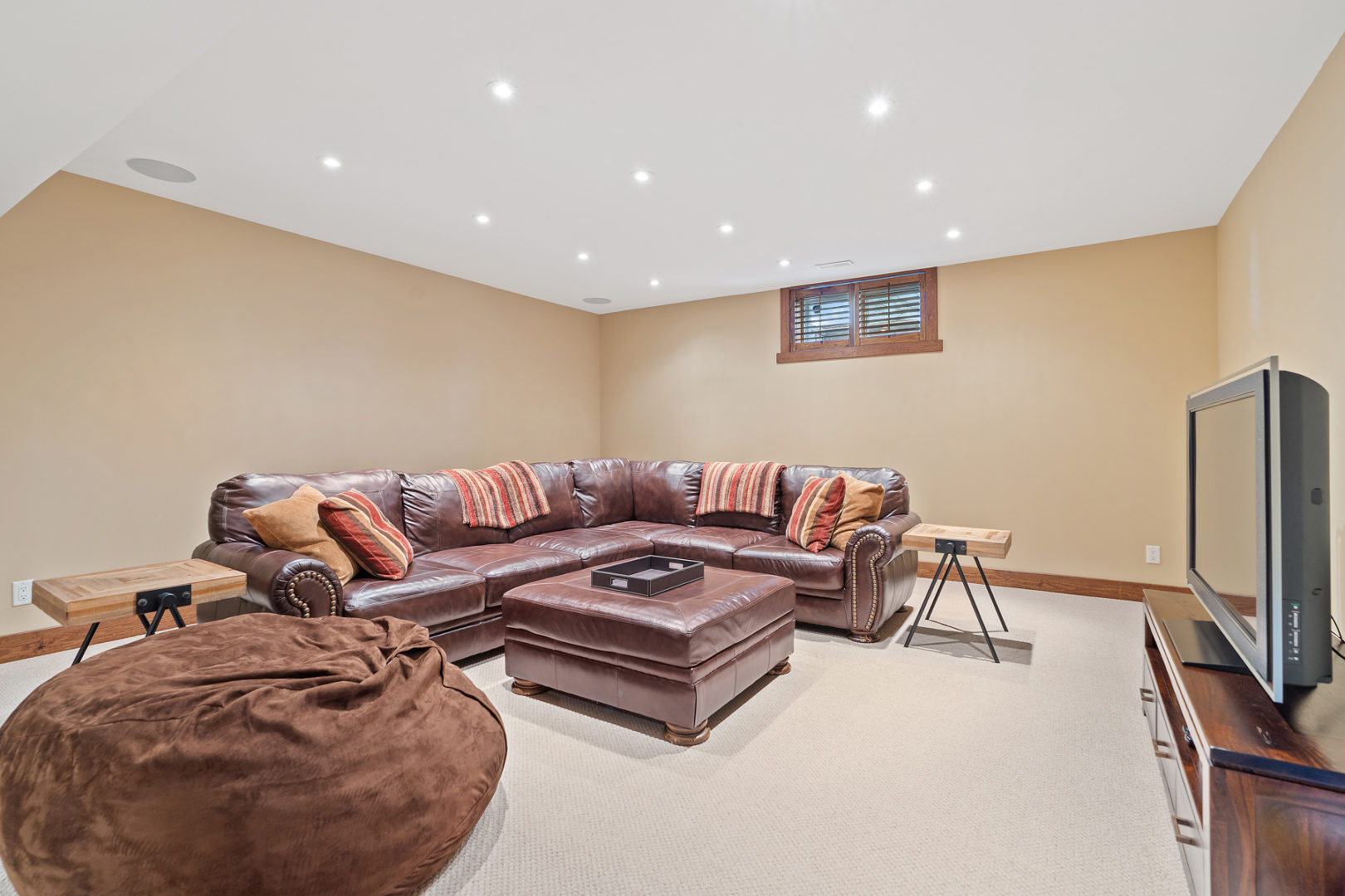 A basement living area in a luxury home with a large leather sectional couch, a beanbag chair, and a television.
