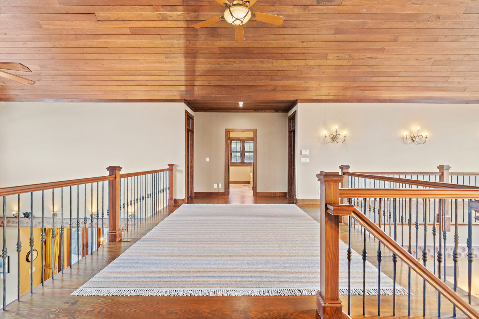 A wide second floor hallway with balconies on both sides looking over the main level of the home.