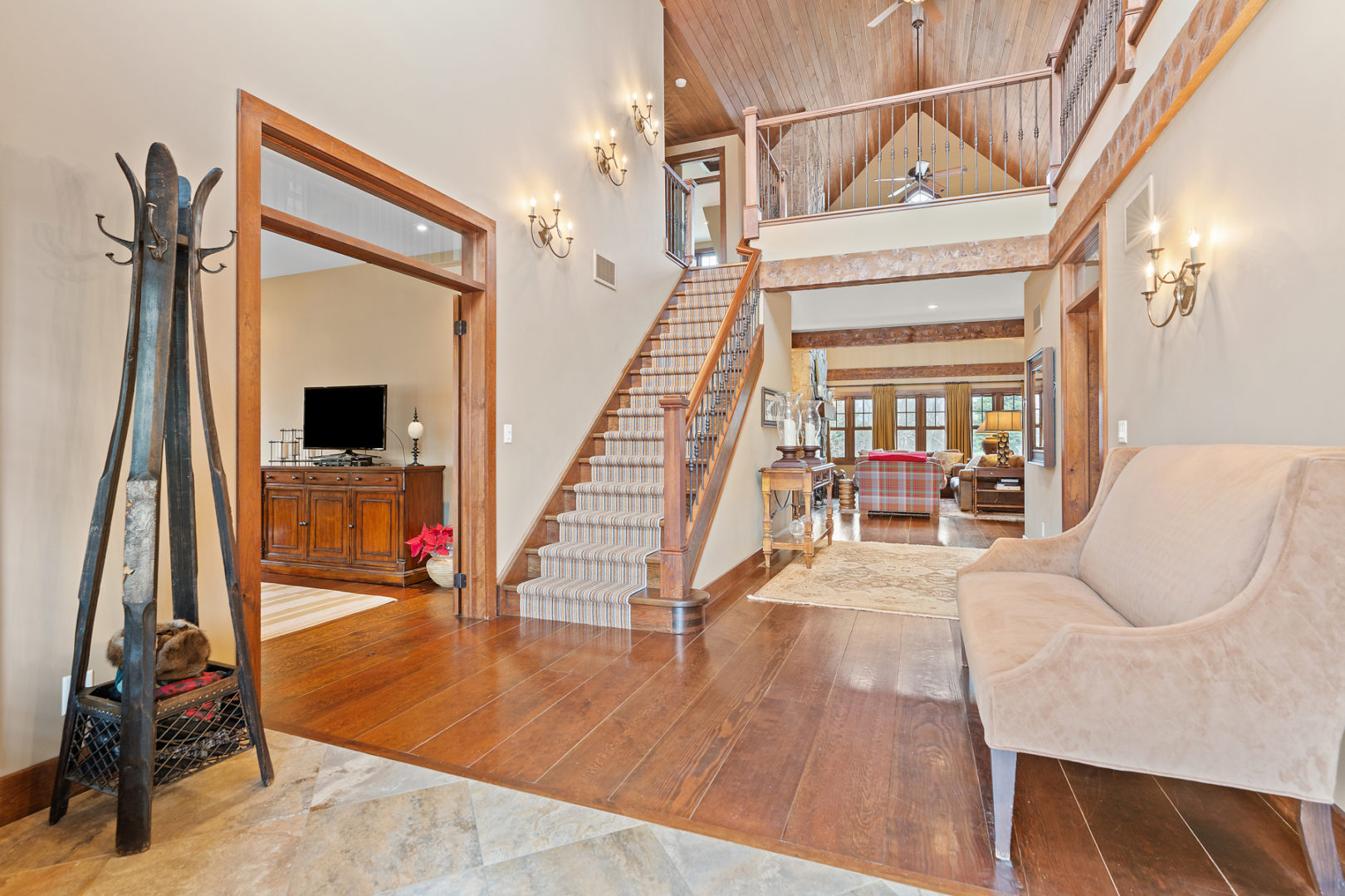 Looking in from the entrance of a luxury home. A hallway leads to a bright living area and a stairway leads up to a second floor hallway with an open balcony.