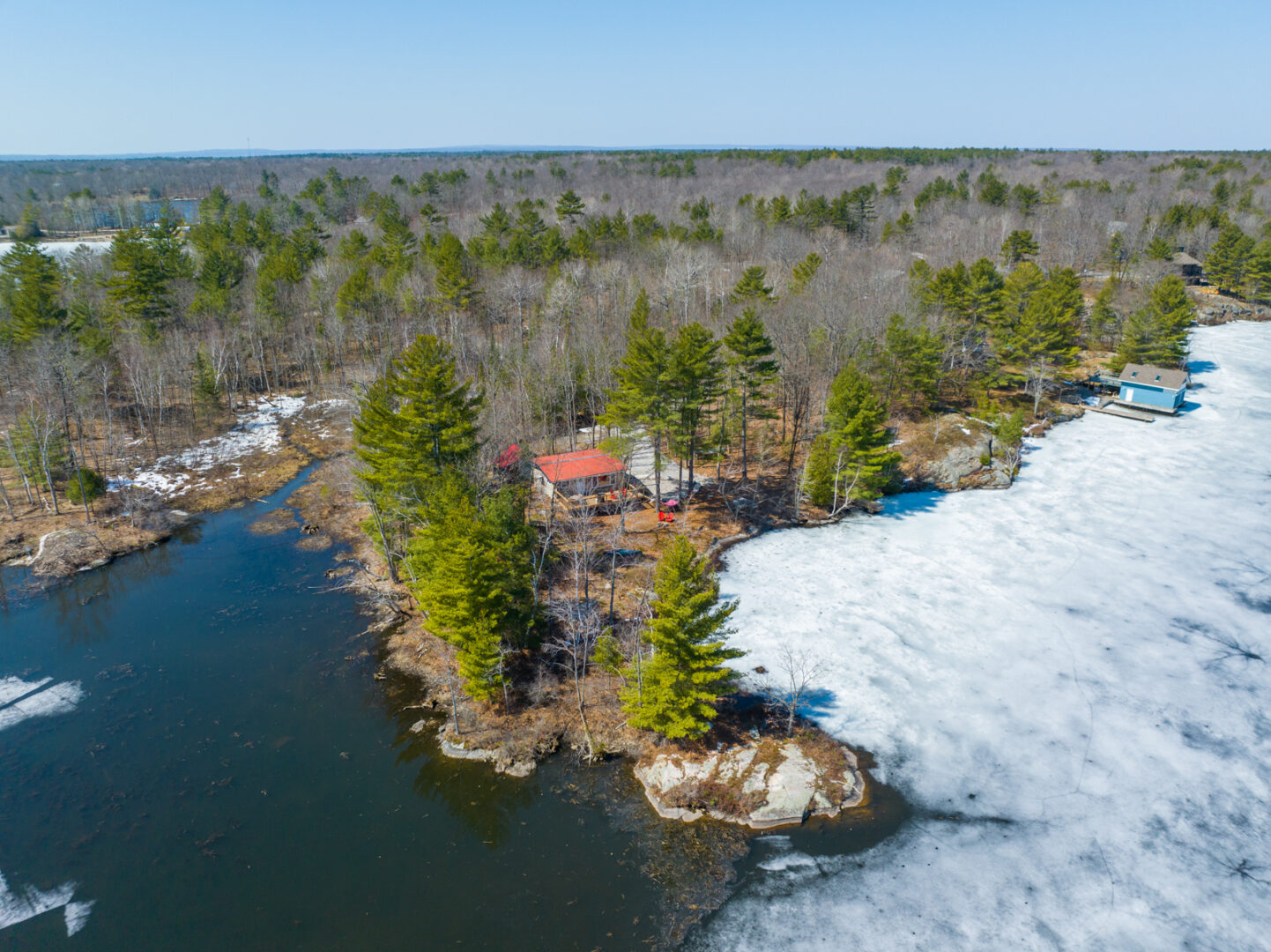 A small peninsula of land surrounded by lake, with a small cottage sitting among the trees on the shoreline.