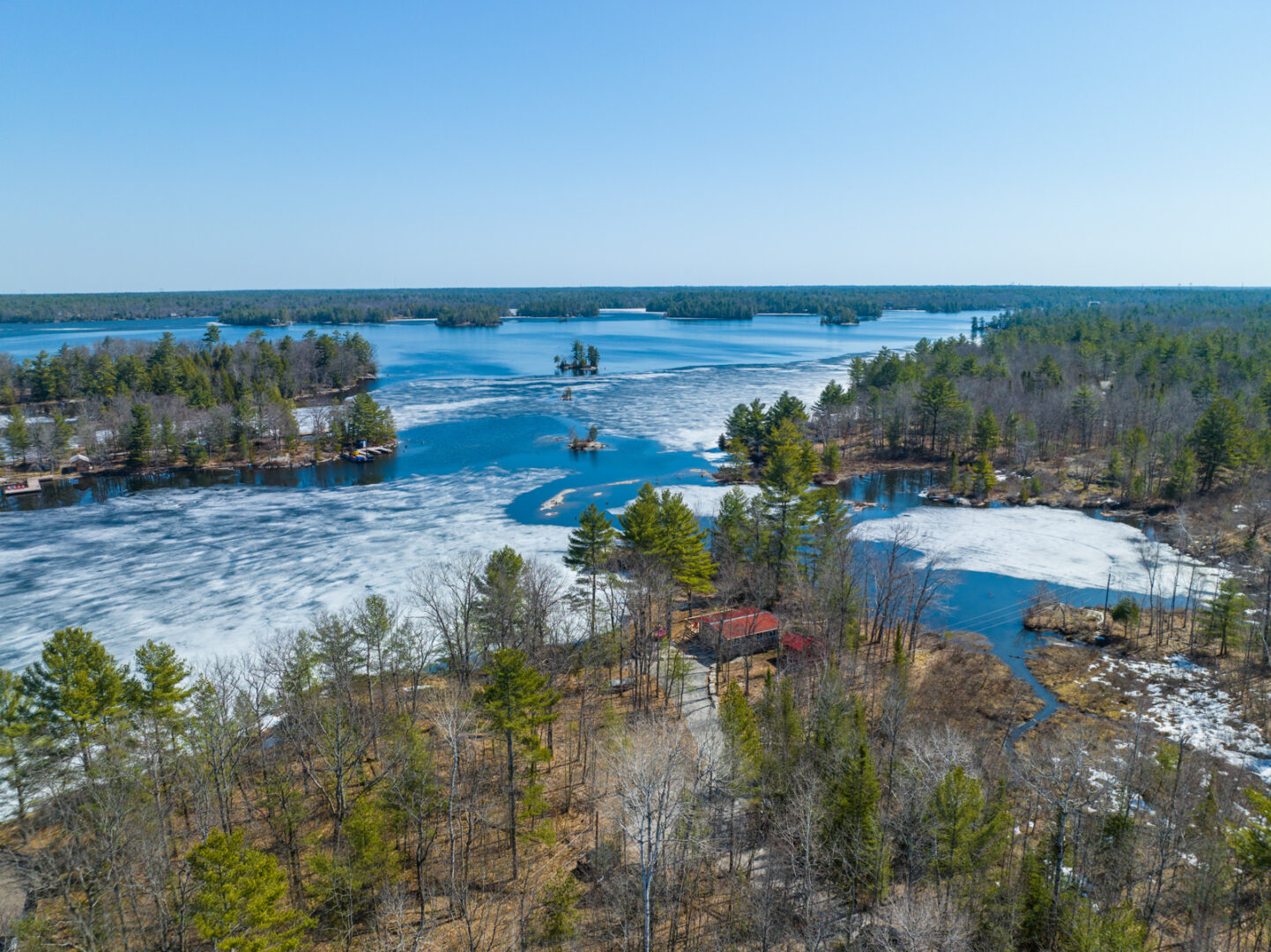 A small peninsula of land surrounded by lake, with a small cottage sitting among the trees on the shoreline.