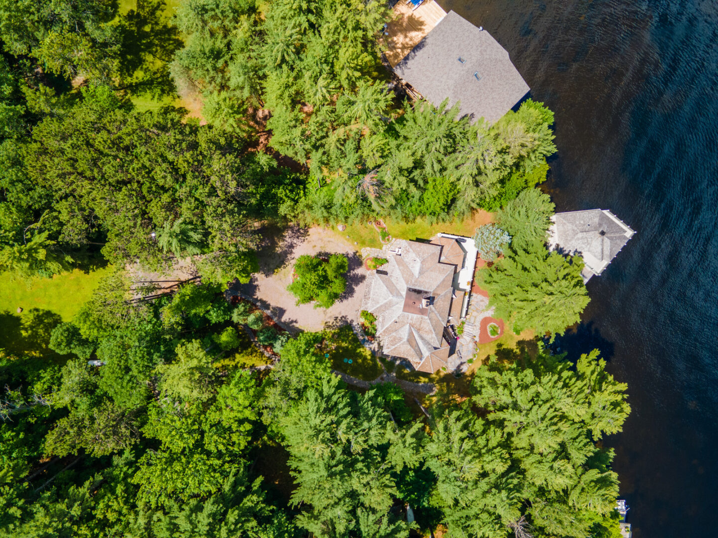 Aerial view of a large cottage property on the water, surrounded by green trees.