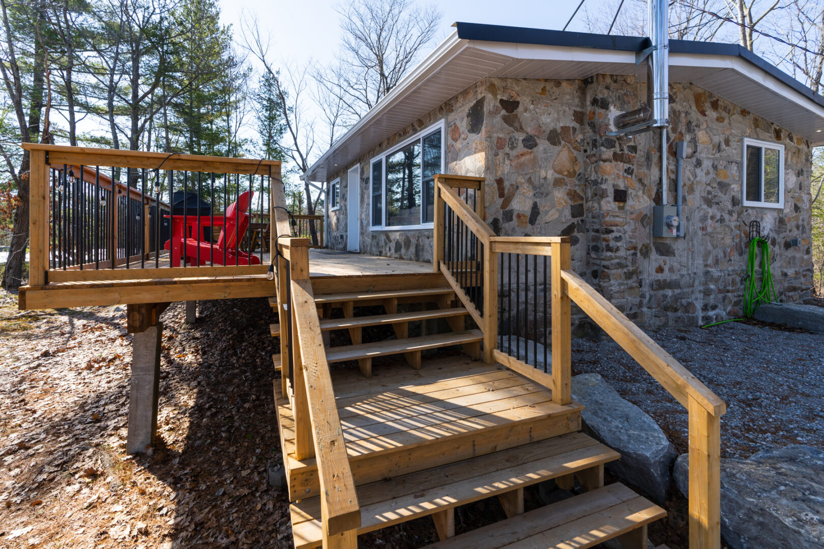 Wooden steps lead up to a new-looking deck branching off the back of a small cottage.