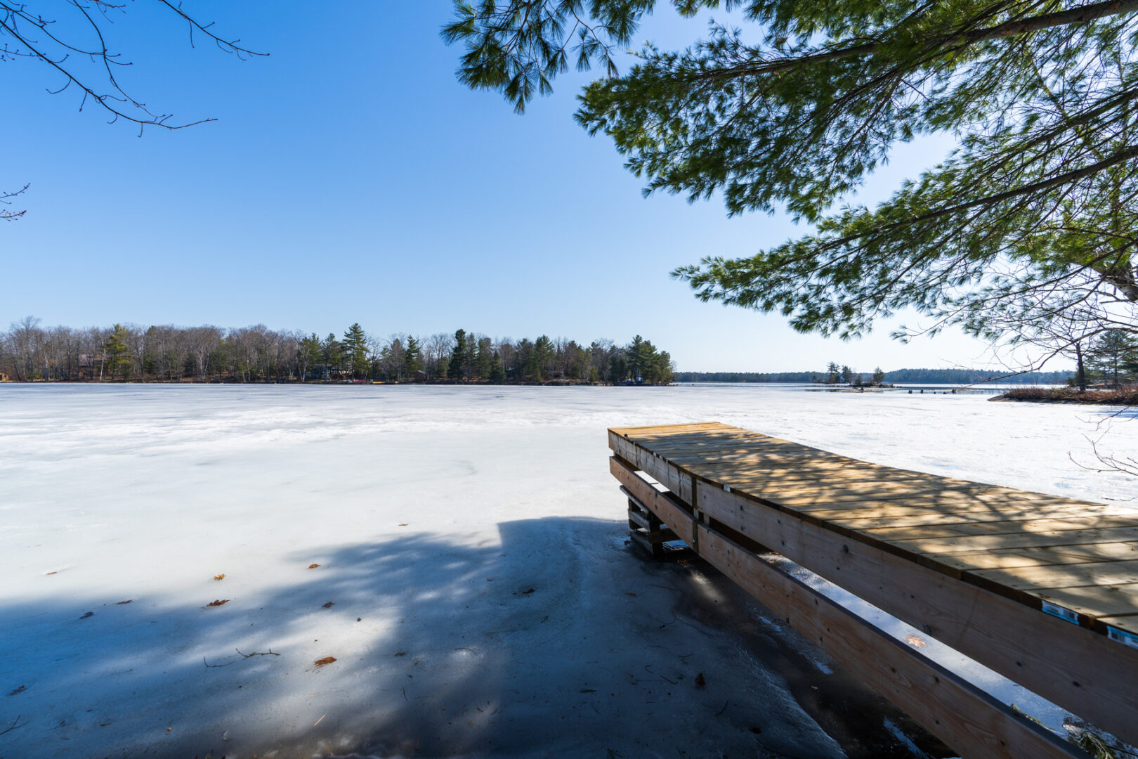 A narrow wooden dock extending into a frozen lake on a sunny day.