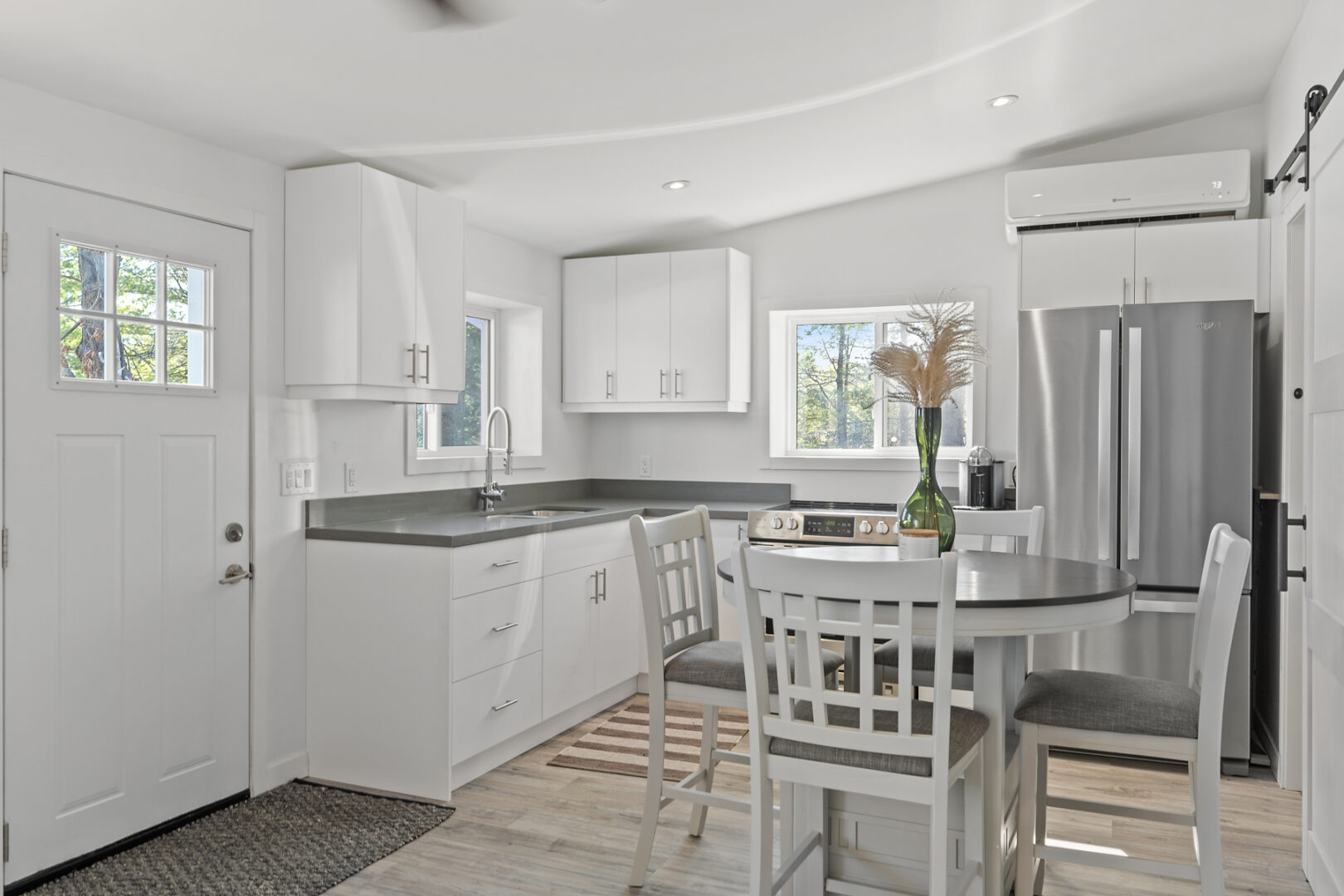 A small, bright, modern kitchen with a round dining table, stainless steel appliances, and white cabinetry.