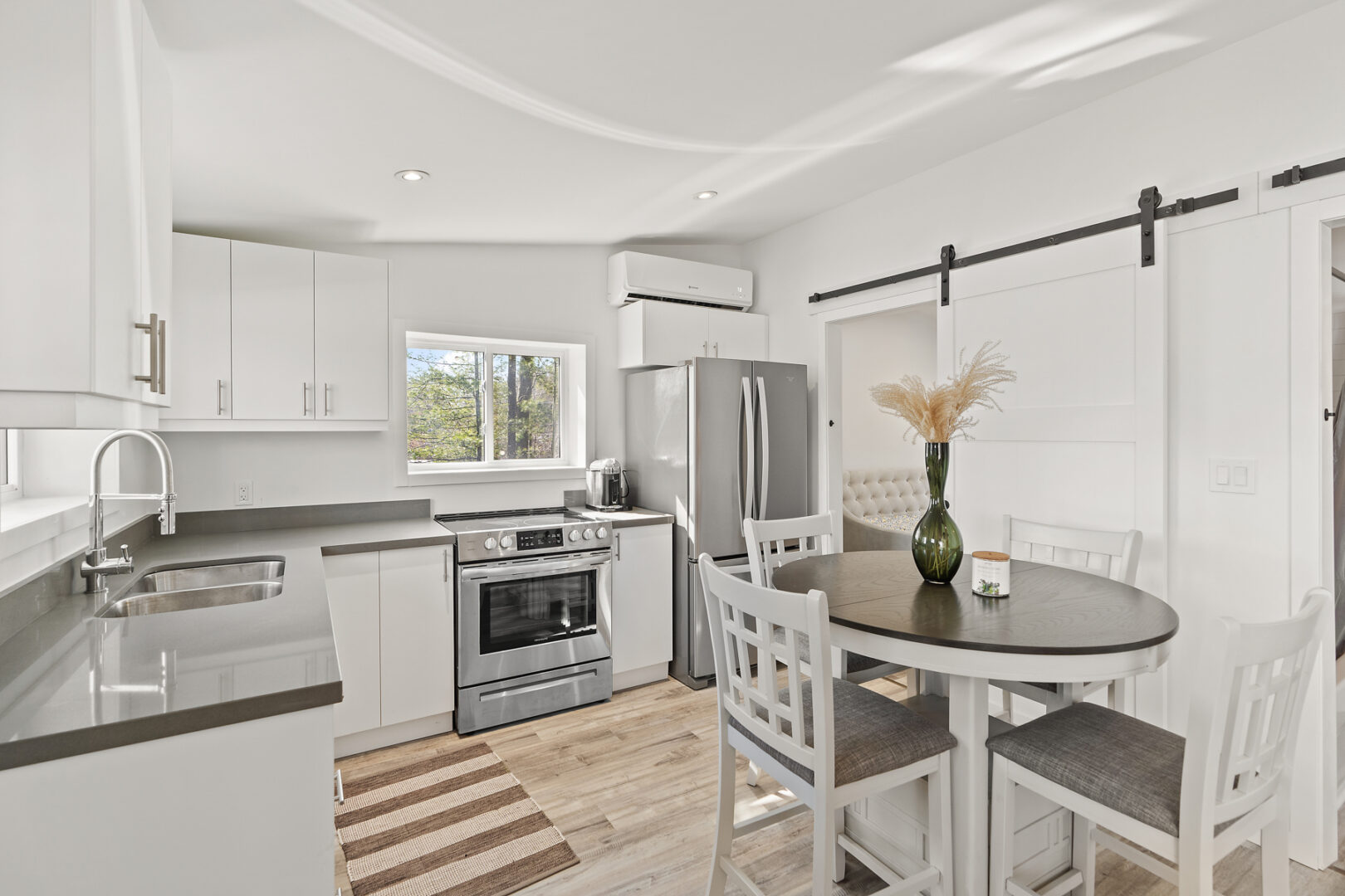 A small, bright, modern kitchen with a round dining table, stainless steel appliances, and white cabinetry.