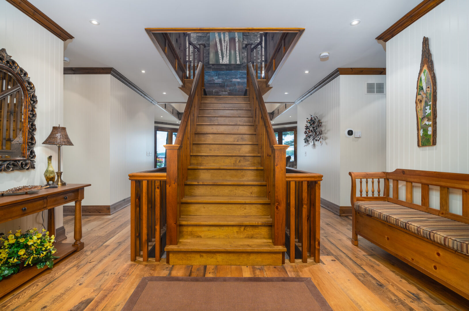 Looking into a large house from the front entrance, a large staircase leads up to a second level.